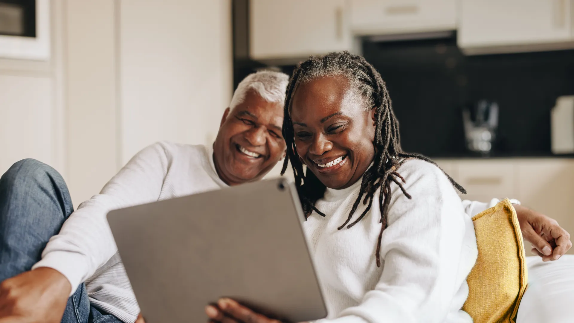 Smiling senior couple sitting on couch using tablet together in cozy home setting