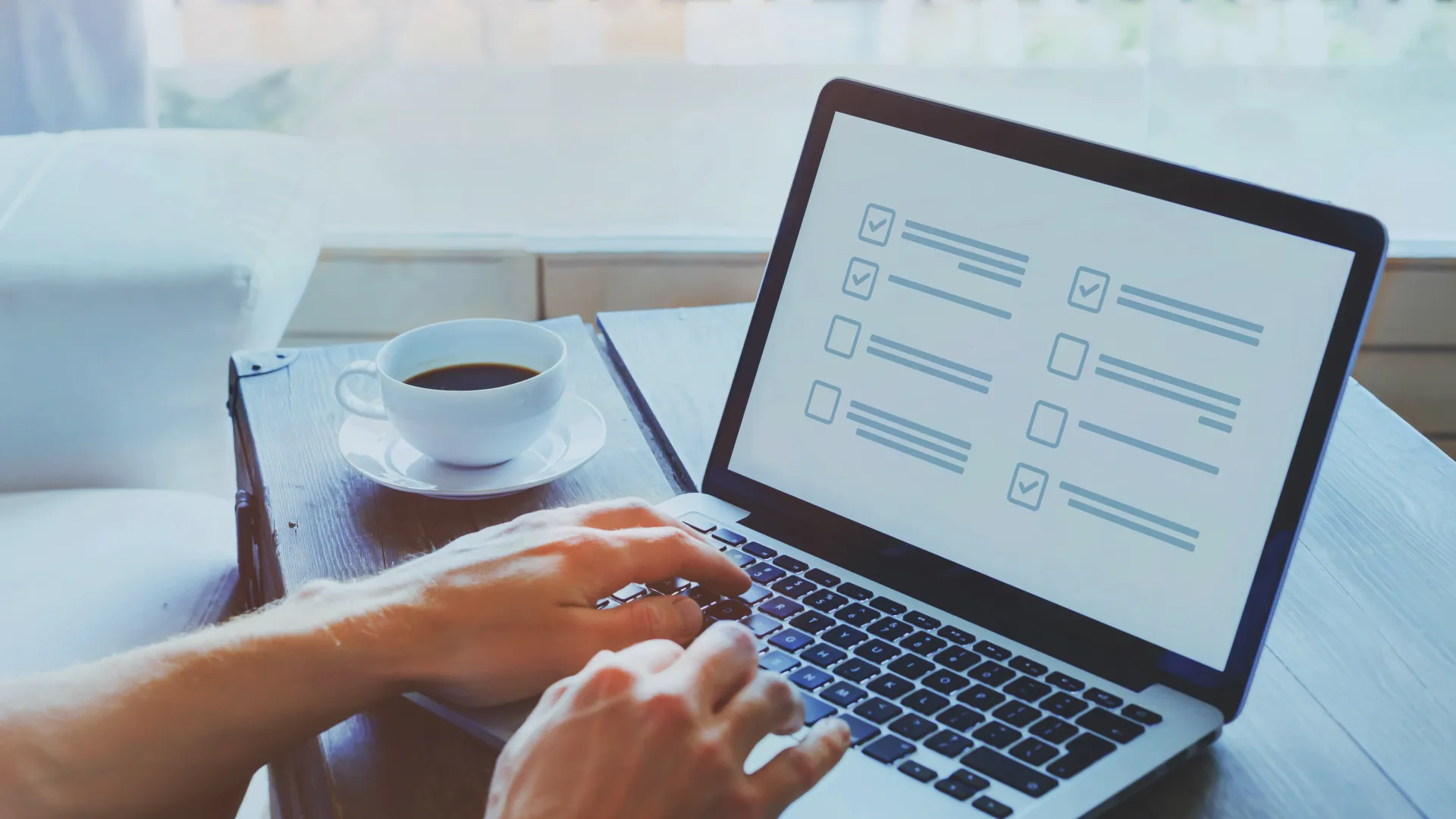 Person completing a checklist on a laptop at a wooden table with a cup of coffee nearby.