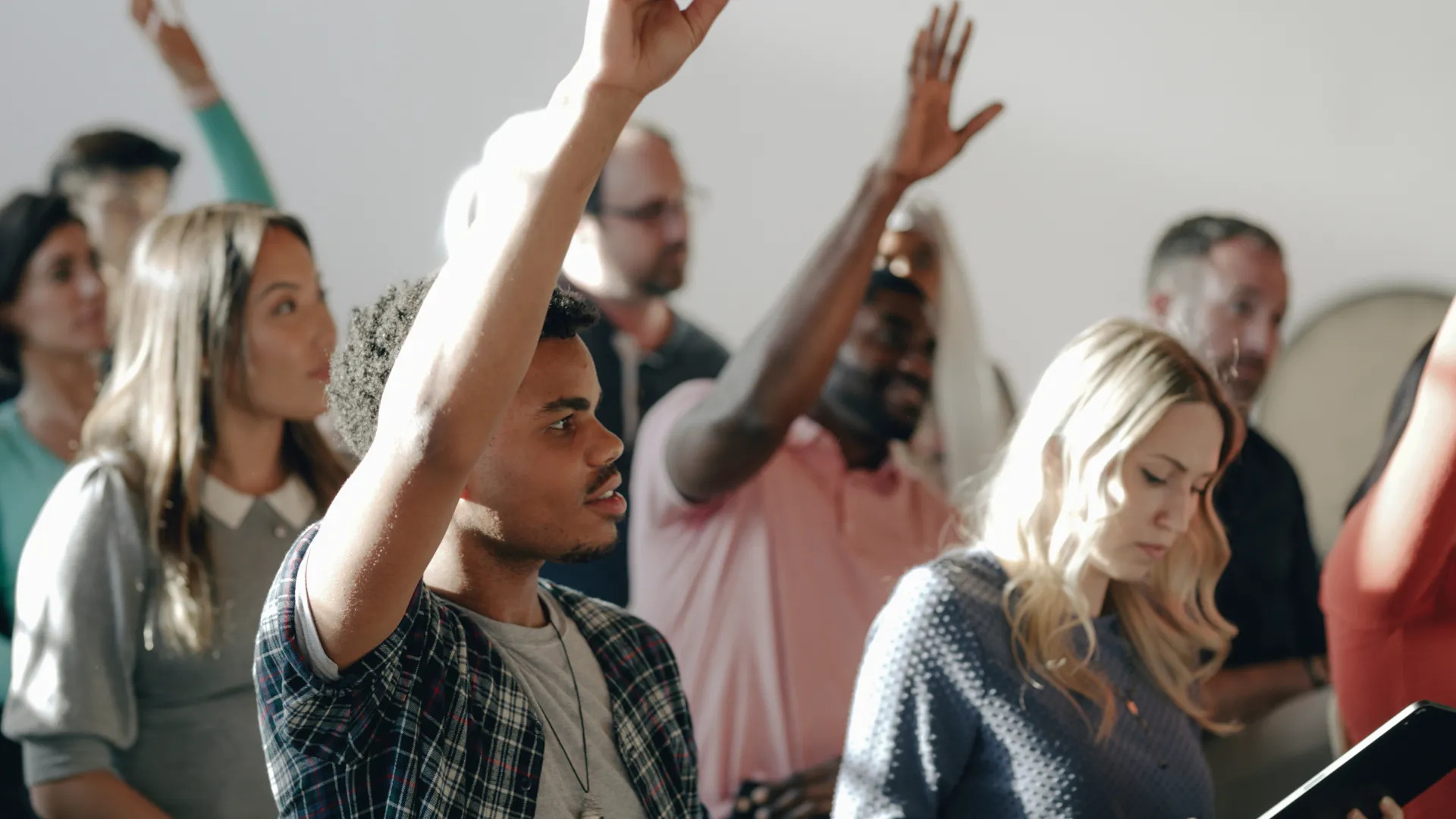 Diverse group of people raising hands during a meeting or classroom setting
