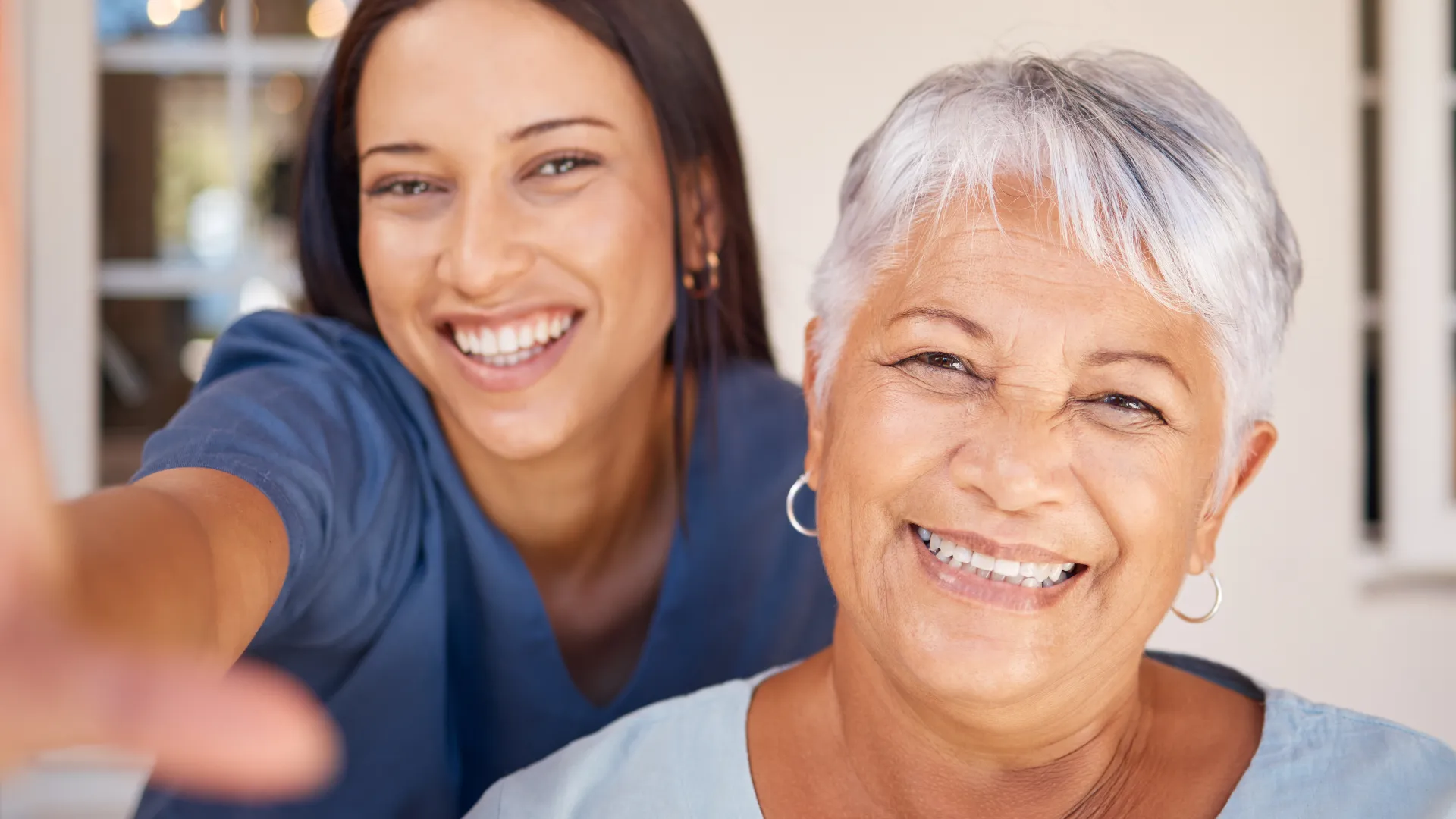 Smiling young woman and elderly woman taking a cheerful selfie together indoors in a bright room