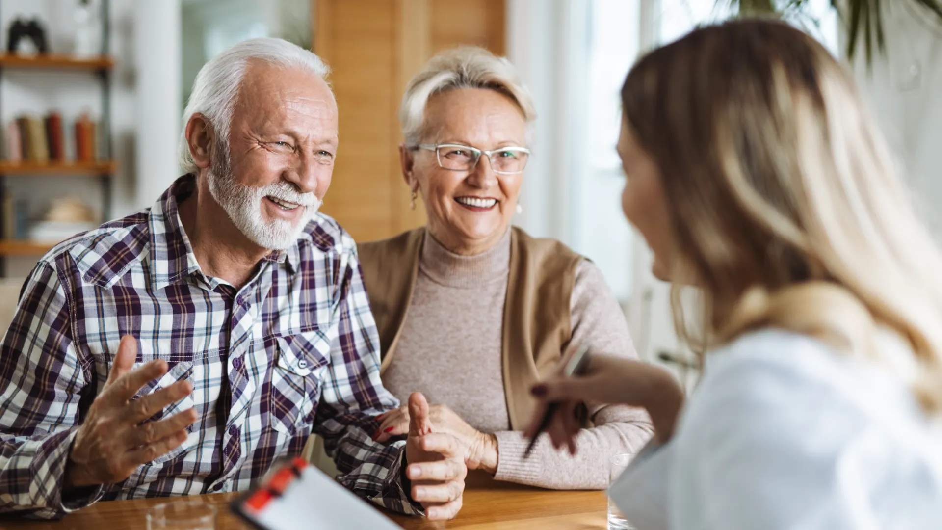 Elderly couple smiling and talking with a professional woman during a consultation at home