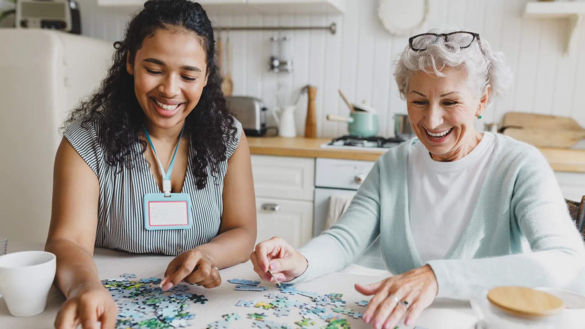 Two women happily assembling a colorful jigsaw puzzle together at a kitchen table.