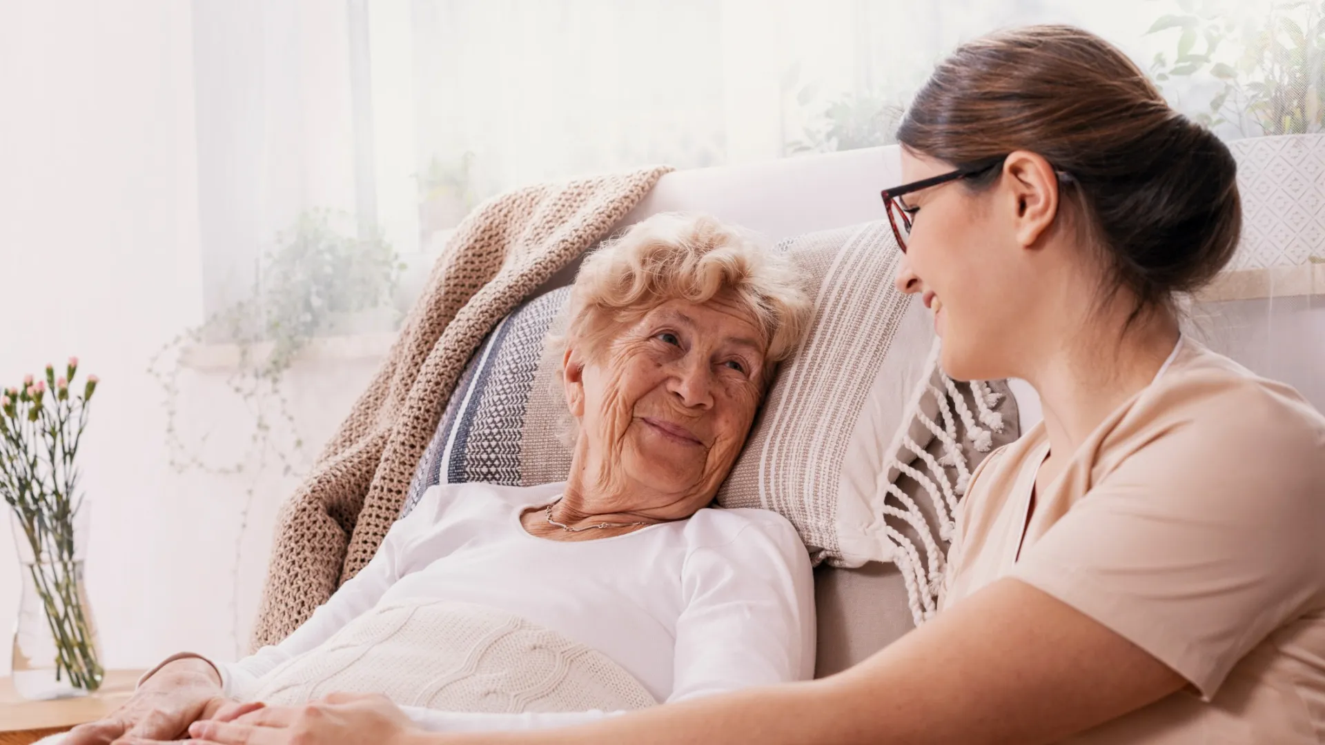 Caregiver and elderly woman share a warm moment in a cozy home setting, emphasizing compassion and companionship.