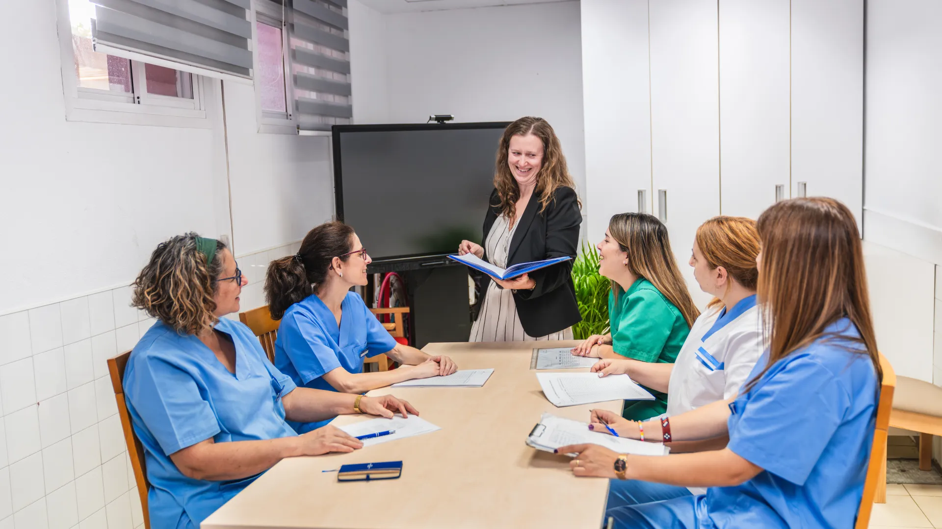 A healthcare meeting with five professionals discussing in a modern clinic setting.