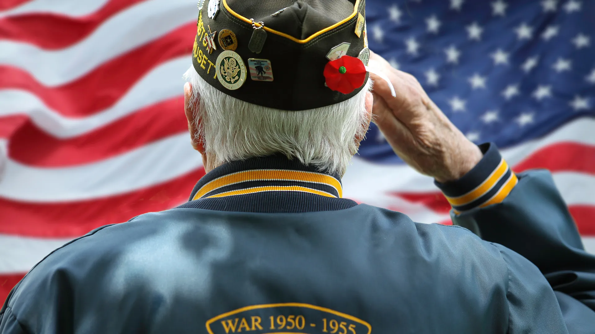 Veteran with Korean War 1950-1955 patch saluting in front of a waving American flag