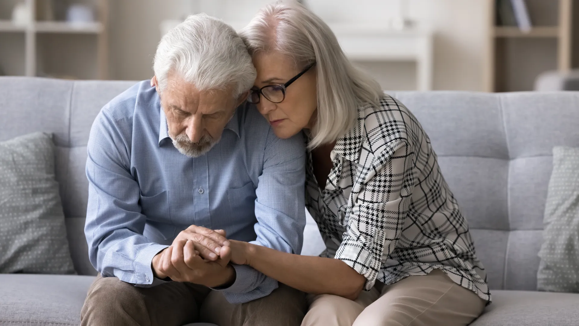 Concerned elderly woman comforting distressed older man sitting on couch at home