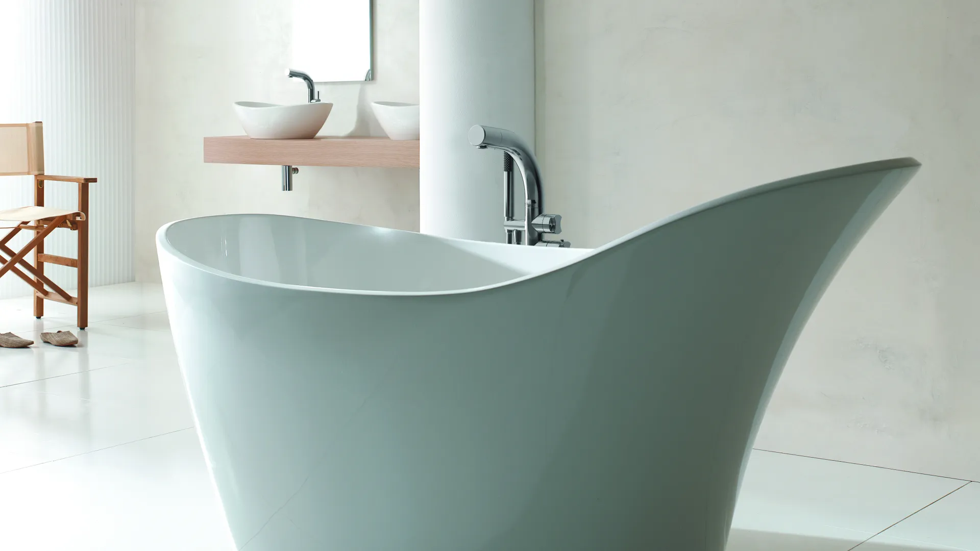 Modern white freestanding bathtub in a minimalist bathroom with light walls and wooden chair.