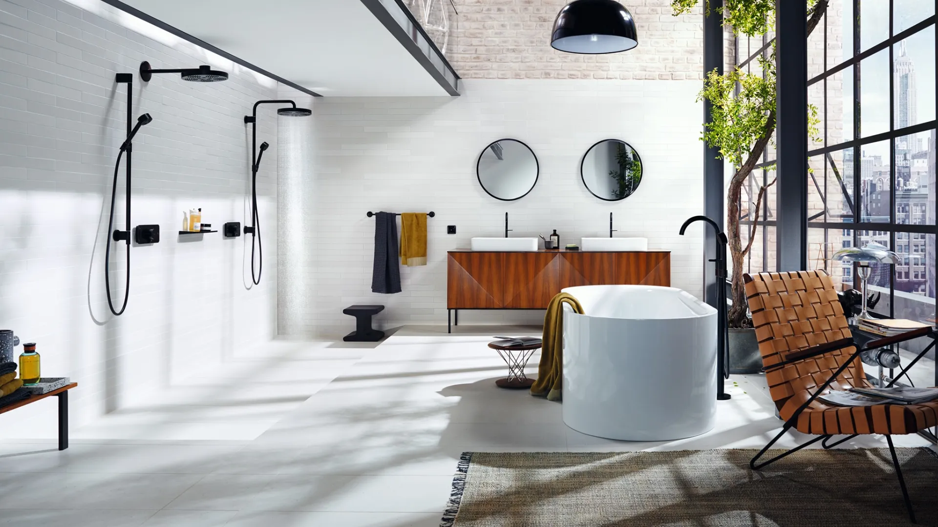 Modern loft-style bathroom with freestanding tub, dual sinks, open showers, large windows, and indoor greenery.