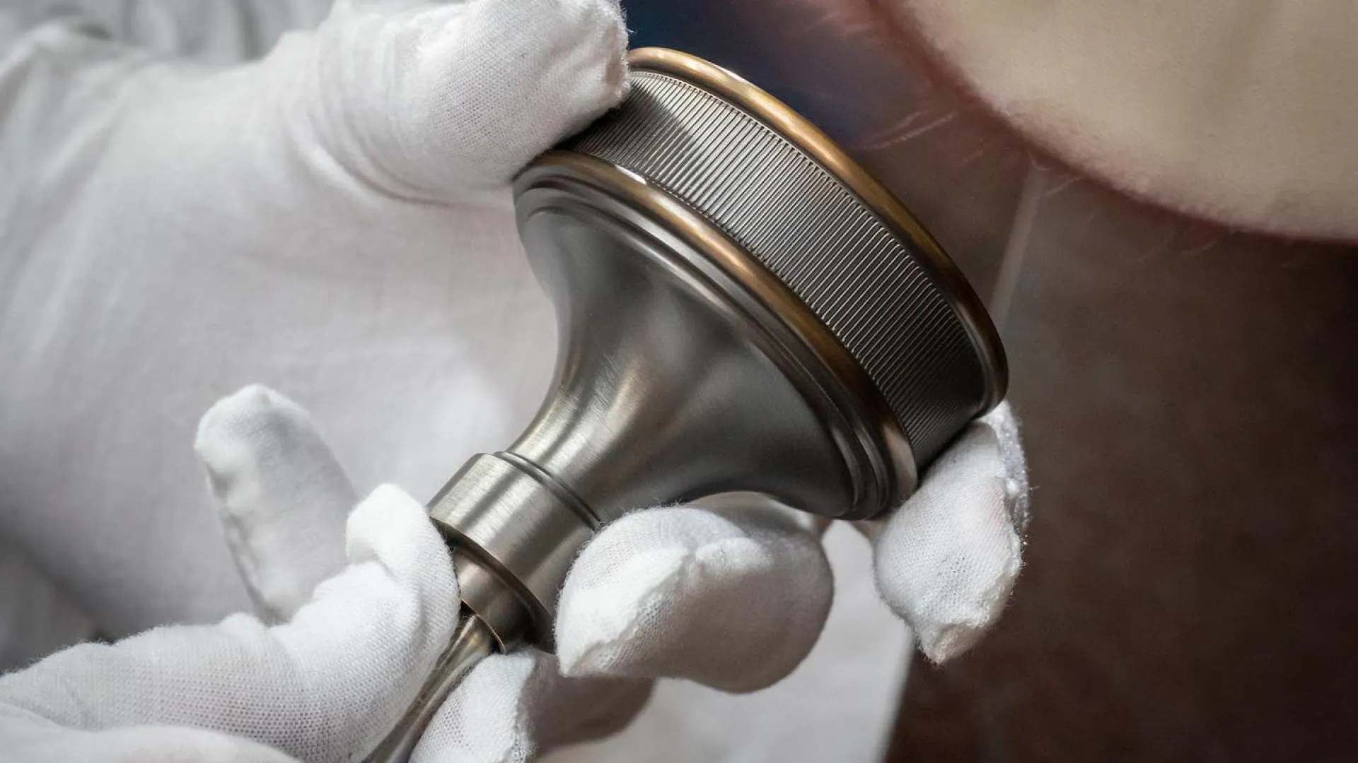 Hand in white gloves polishing a metal door knob with a buffing wheel to achieve a smooth finish