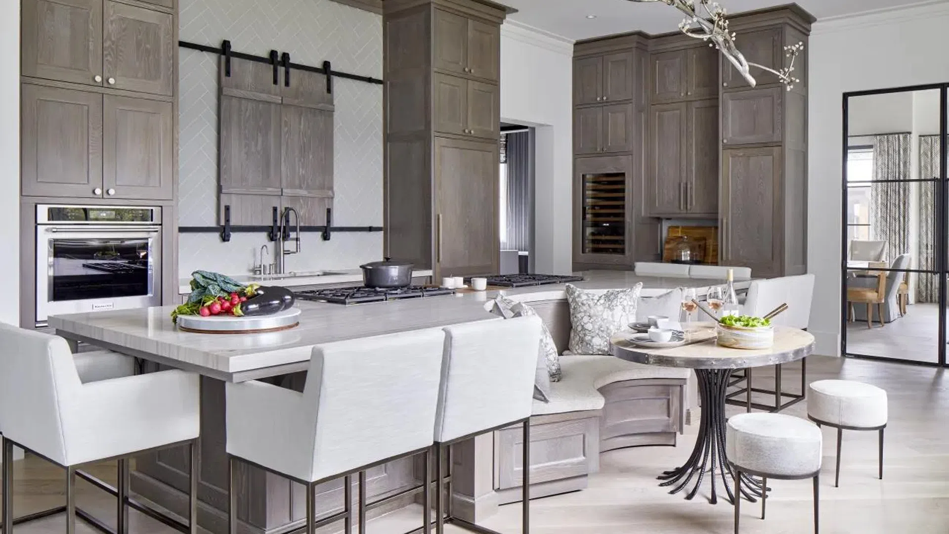 Modern kitchen with gray cabinetry, built-in appliances, large island, breakfast nook, and contemporary lighting fixture