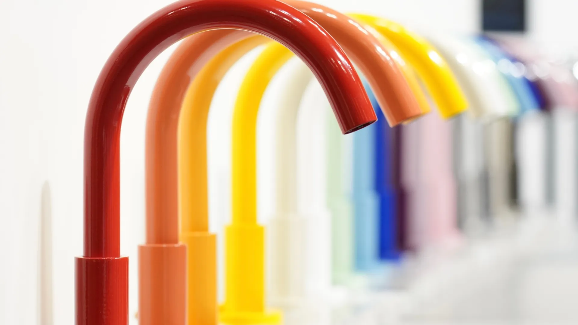 Row of colorful modern faucets in red, orange, yellow, blue, and other shades displayed on a white counter.