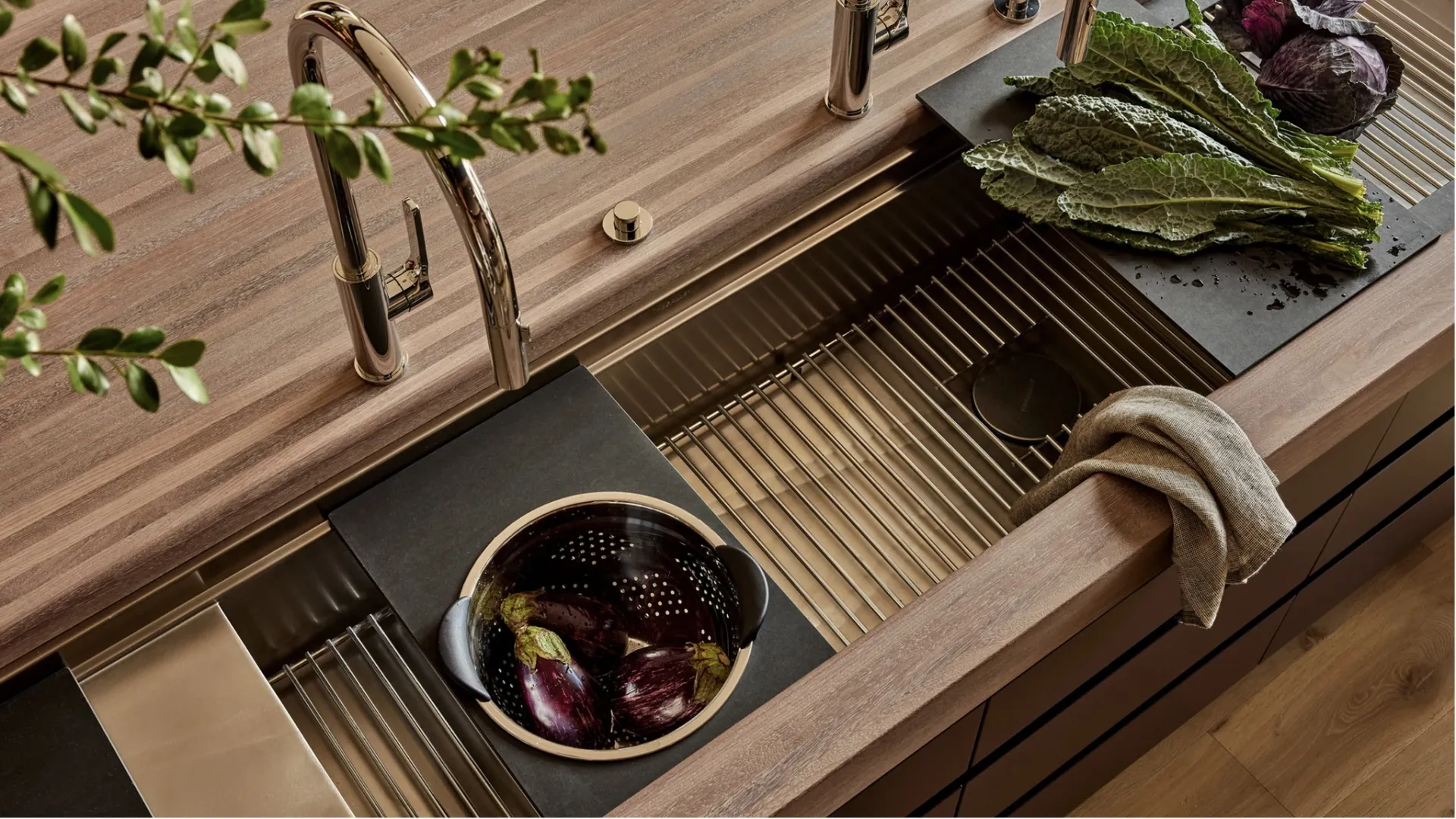 Modern kitchen sink with polished faucet, wooden countertop, leafy greens, and purple cabbages on cutting boards.