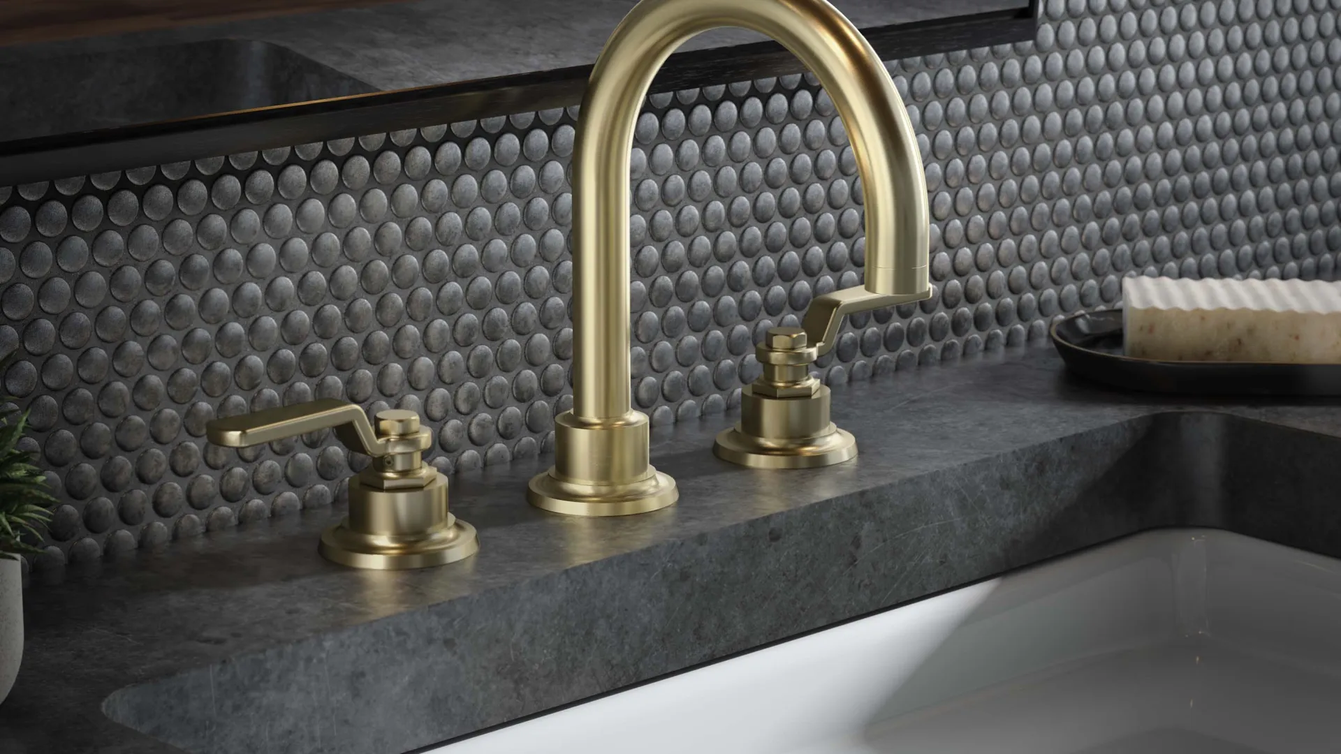 Modern bathroom sink with matte gold faucet and dark stone countertop against a textured tile backsplash.
