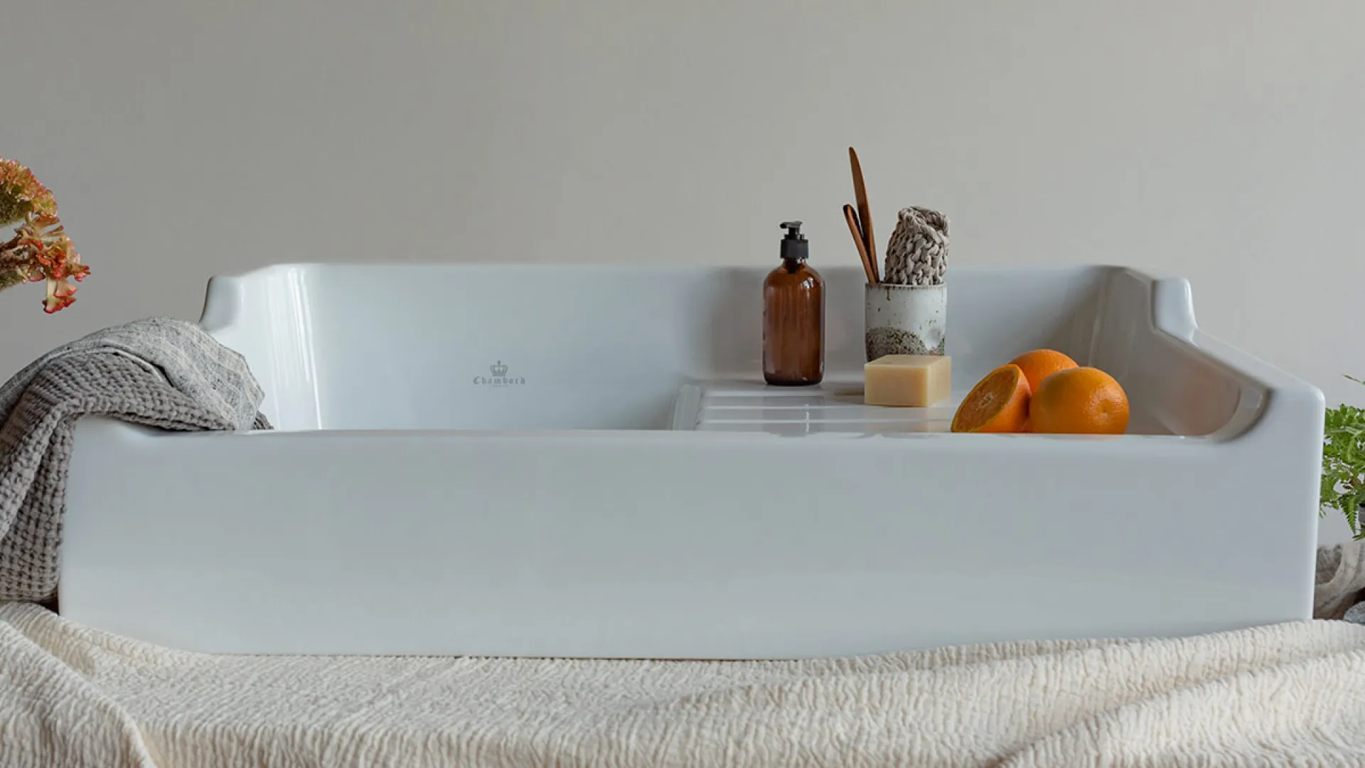 White elegant bathtub with towel, brown bottle, soap, oranges, and wooden brush in minimalist bathroom.