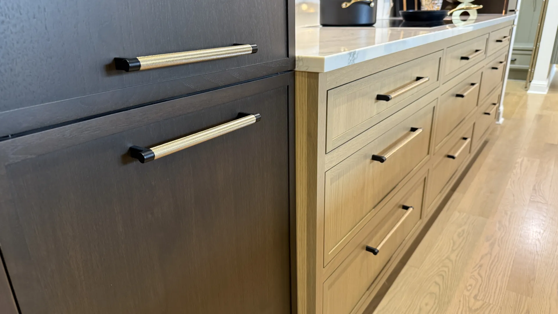 Modern kitchen cabinets with two-tone wood finish and brass handles under a white countertop on hardwood floor.