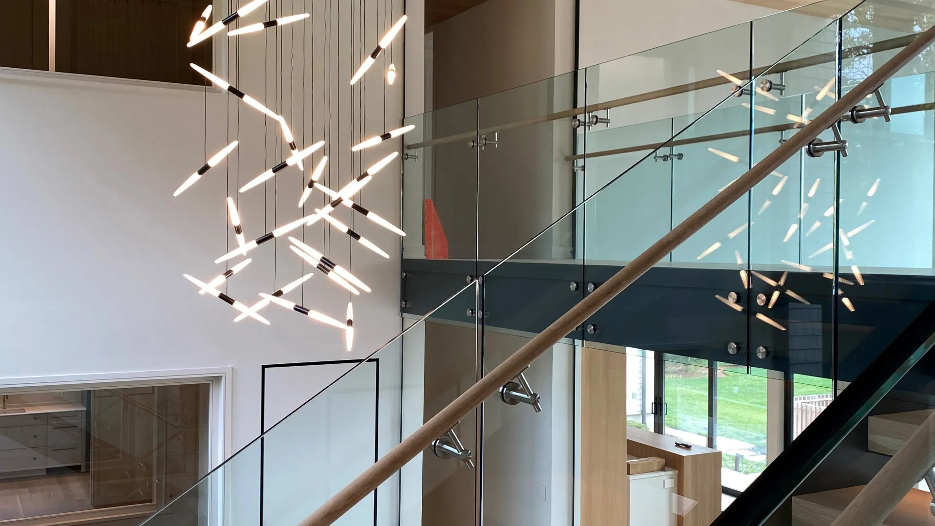 Modern staircase with glass railings and a contemporary pendant light fixture in a spacious interior.