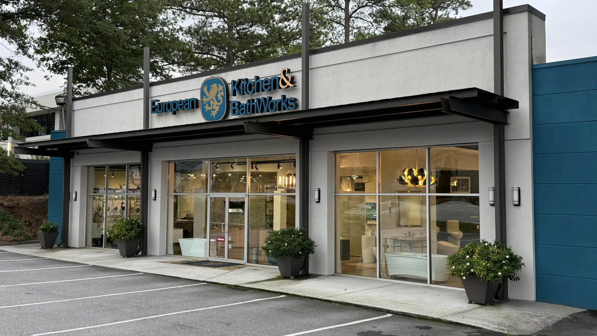Modern European Kitchen & BathWorks storefront with large glass windows and potted plants in an empty parking lot.