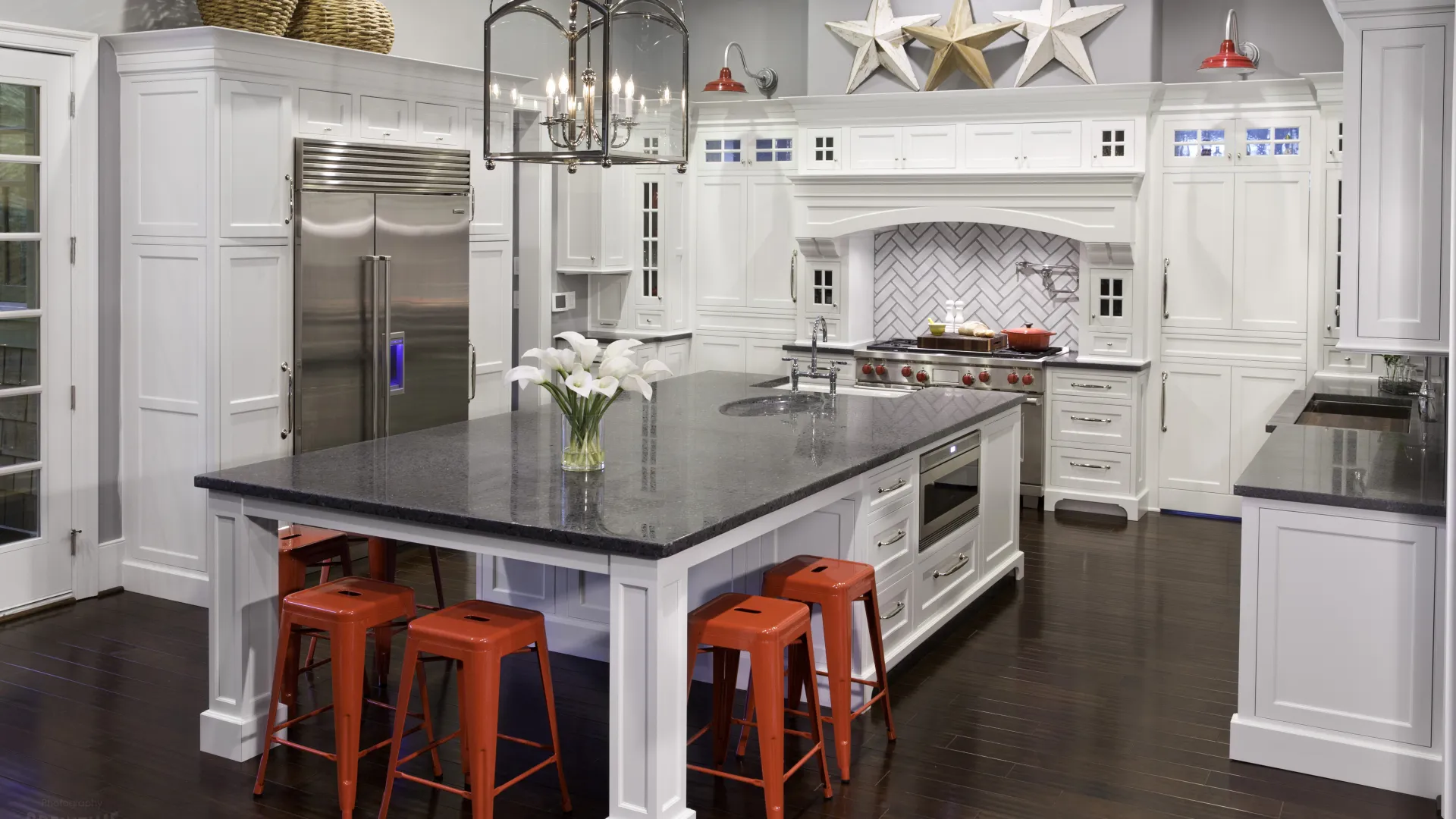 Modern kitchen with large white island, black countertop, red stools, stainless steel appliances, and star wall decor.