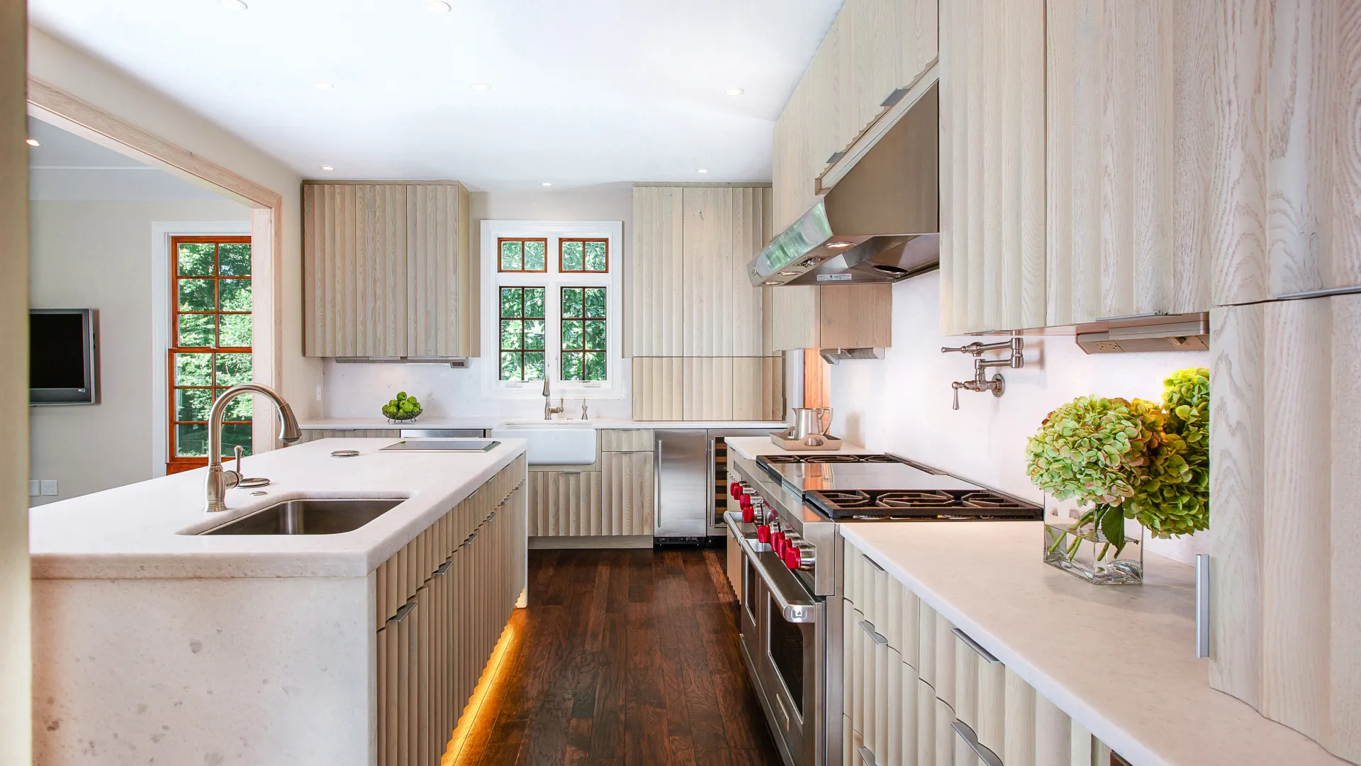 Bright modern kitchen with wooden cabinets, white countertops, stainless steel appliances, and hardwood floors.