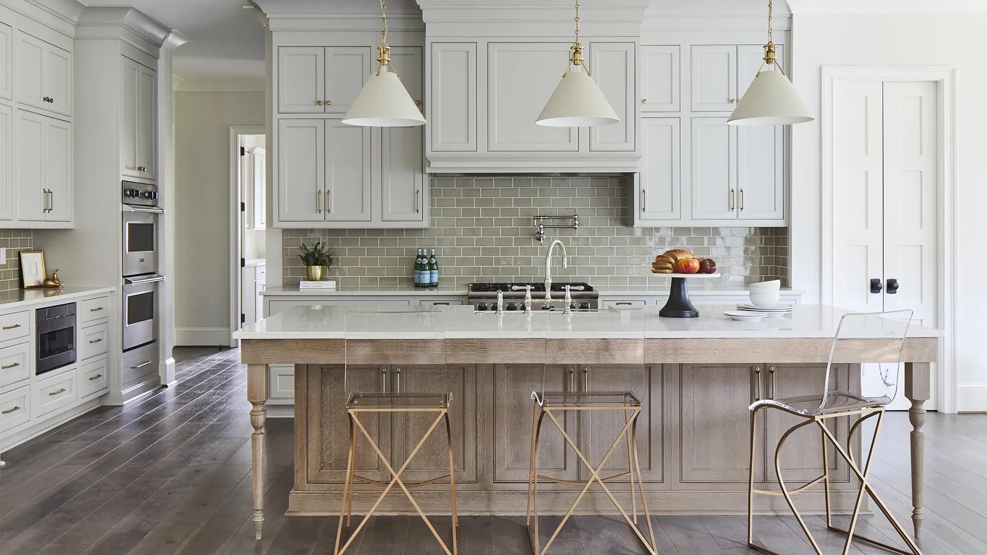 Bright modern kitchen with white cabinetry, large island with wooden base, and three unique metal stools.
