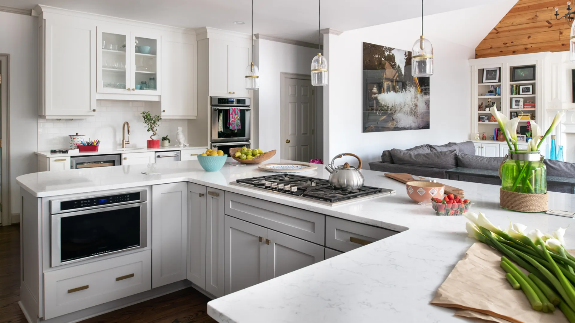 Modern white kitchen with marble countertops, stainless steel appliances, and a view into a cozy living room.