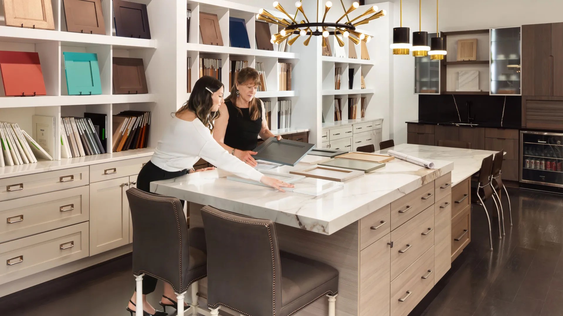 Two women collaborating at a modern kitchen design workspace with stylish materials and vibrant lighting.