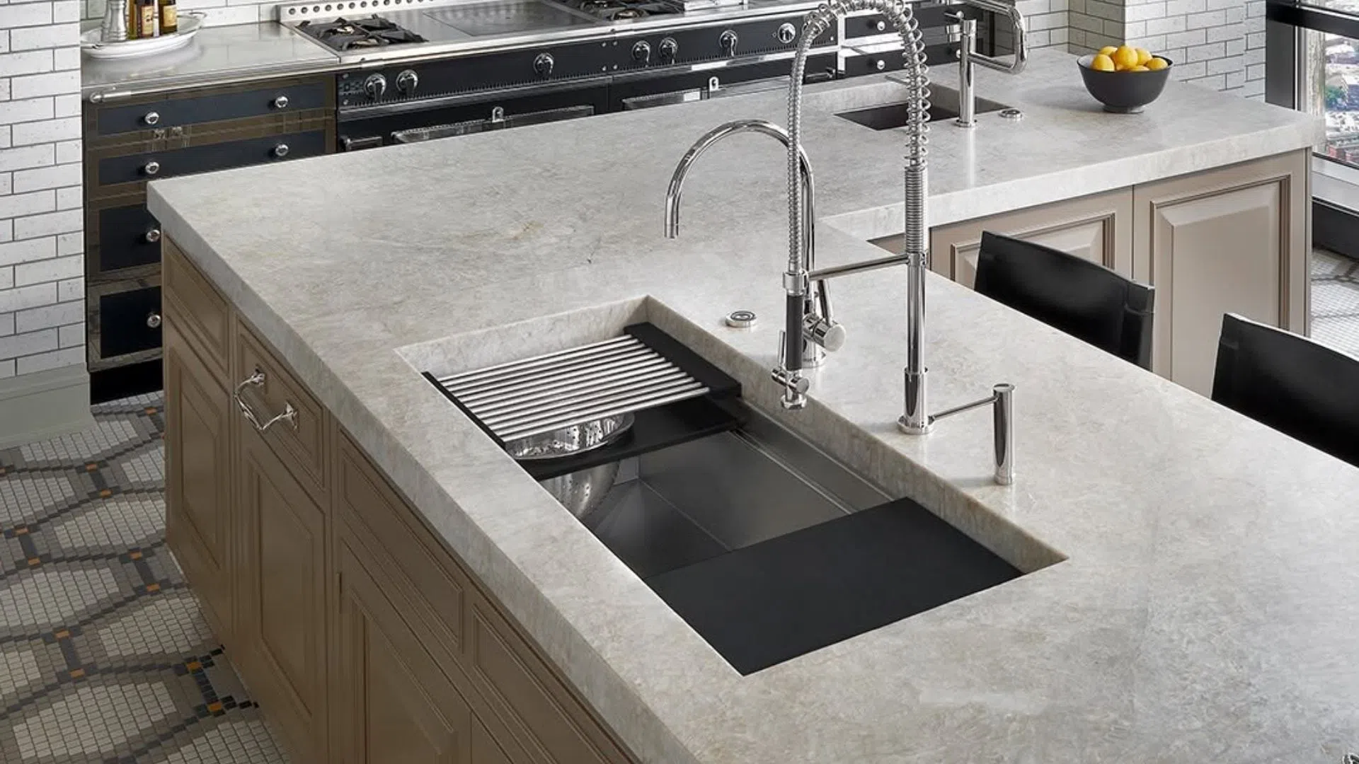 Modern kitchen island with large gray countertop, stainless steel sink, and dual chrome faucets.