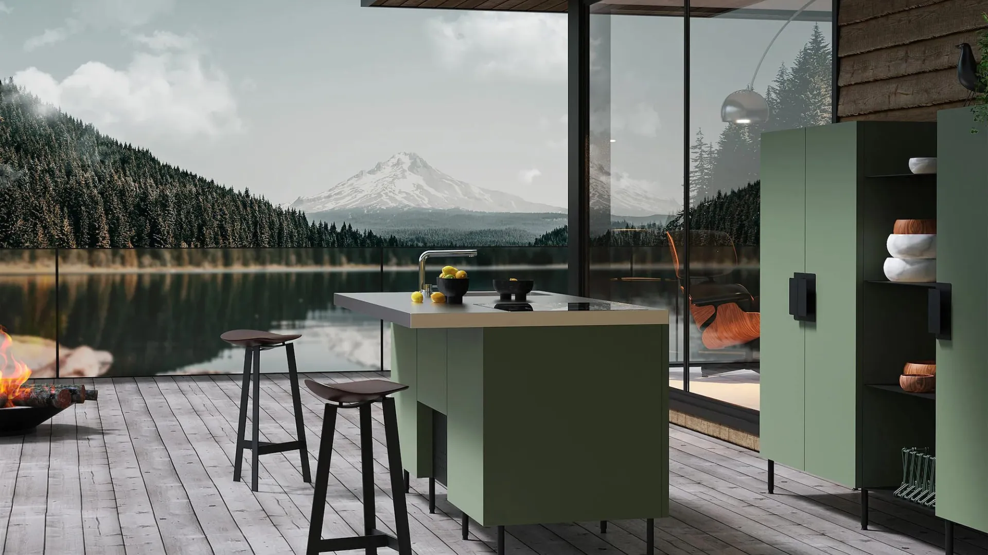 Modern outdoor kitchen with green cabinets overlooks serene lake and snow-capped mountain landscape under cloudy sky