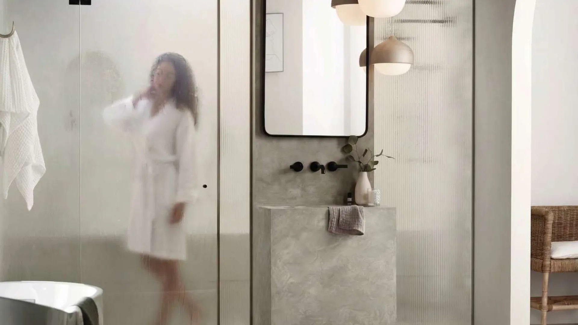 Modern bathroom with concrete sink, frosted glass shower, pendant lights, and a person in a bathrobe inside shower.