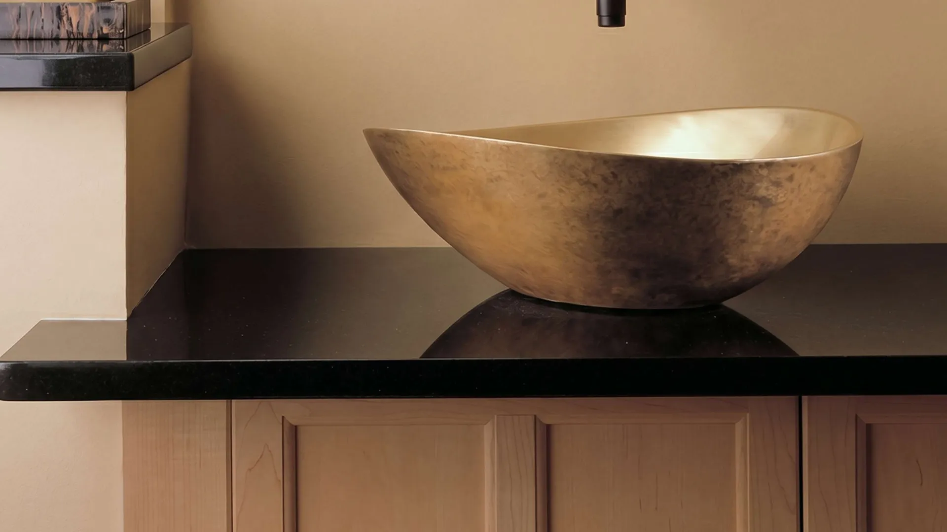 Modern bathroom with a unique gold stone sink, black countertop, black wall-mounted faucet, and beige walls.