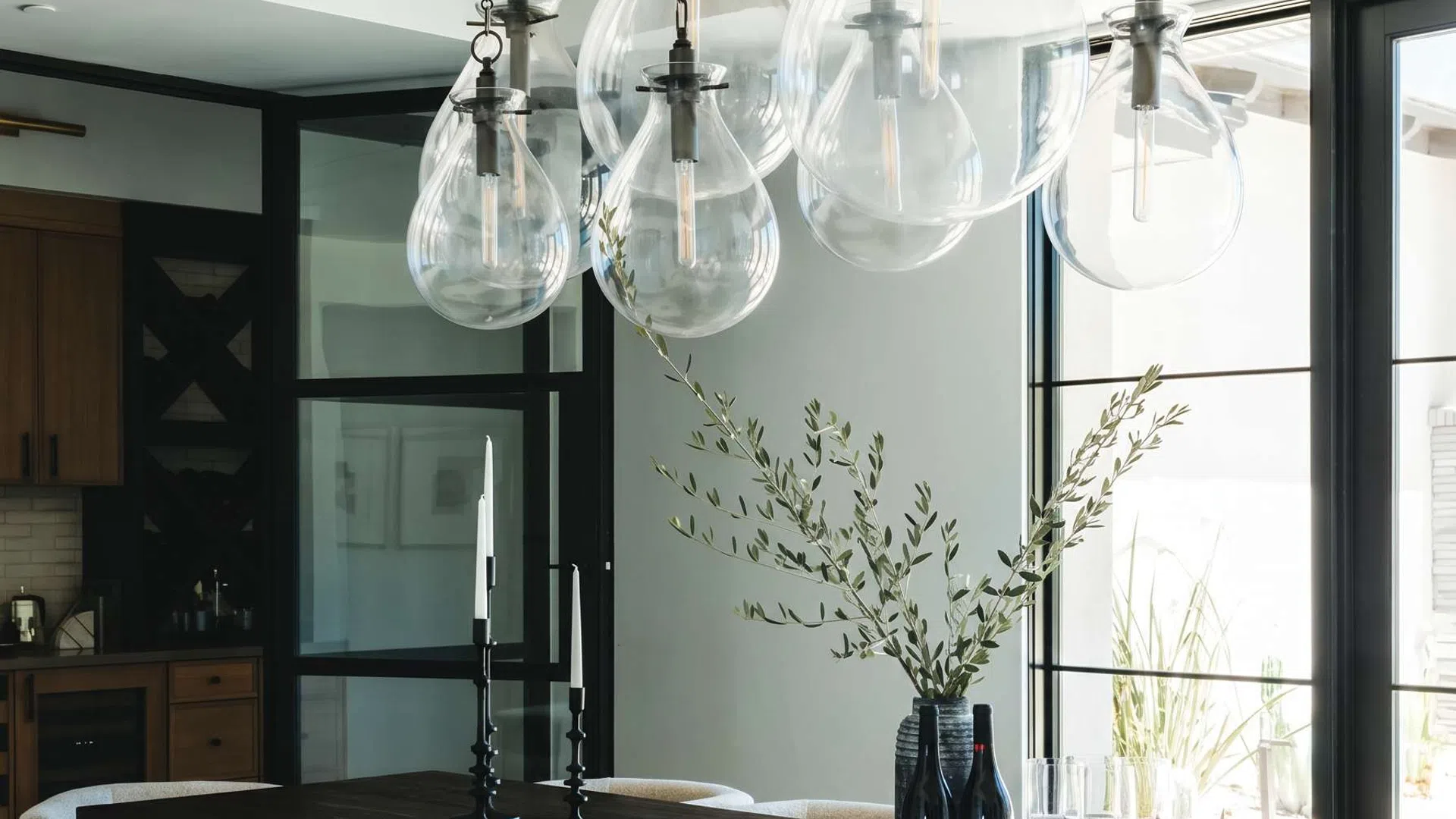 Modern dining room with large dark wood table, beige upholstered chairs, and hanging glass pendant lights.