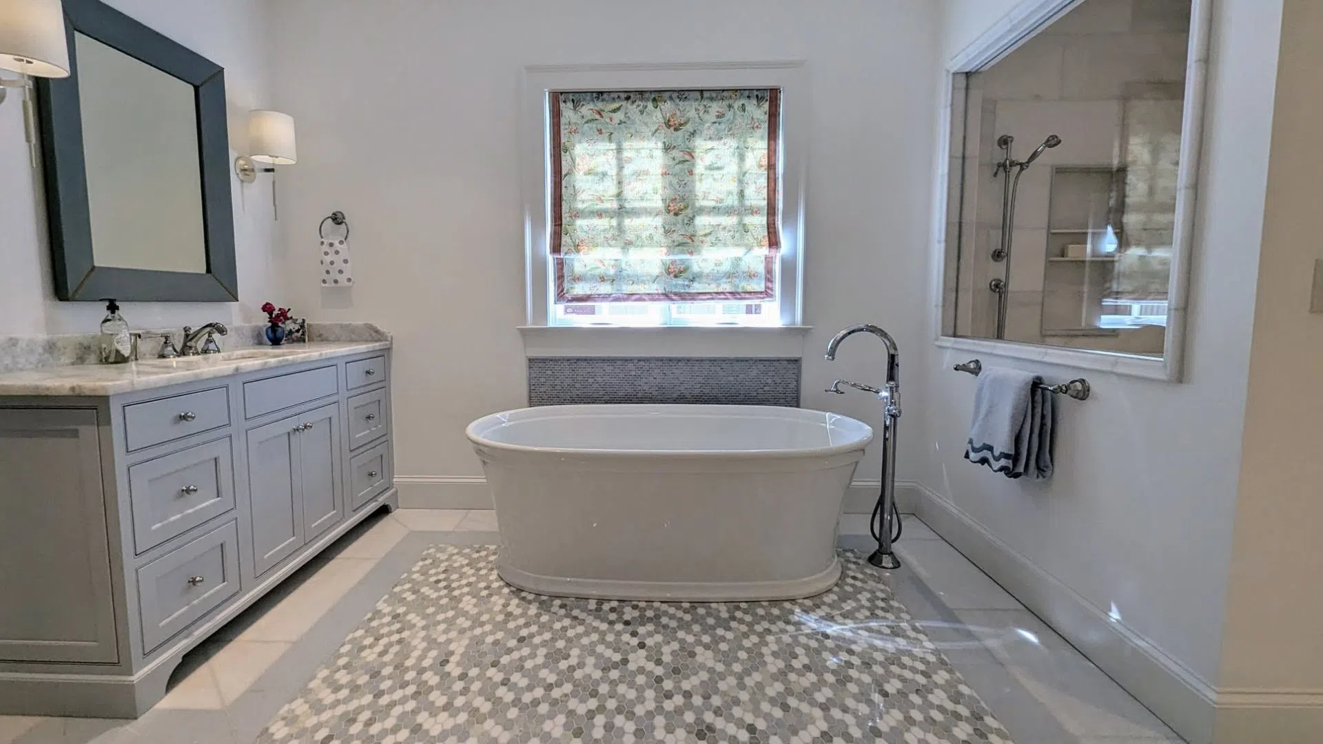 Modern bathroom with freestanding bathtub, patterned tile floor, gray vanity, and floral window shade.
