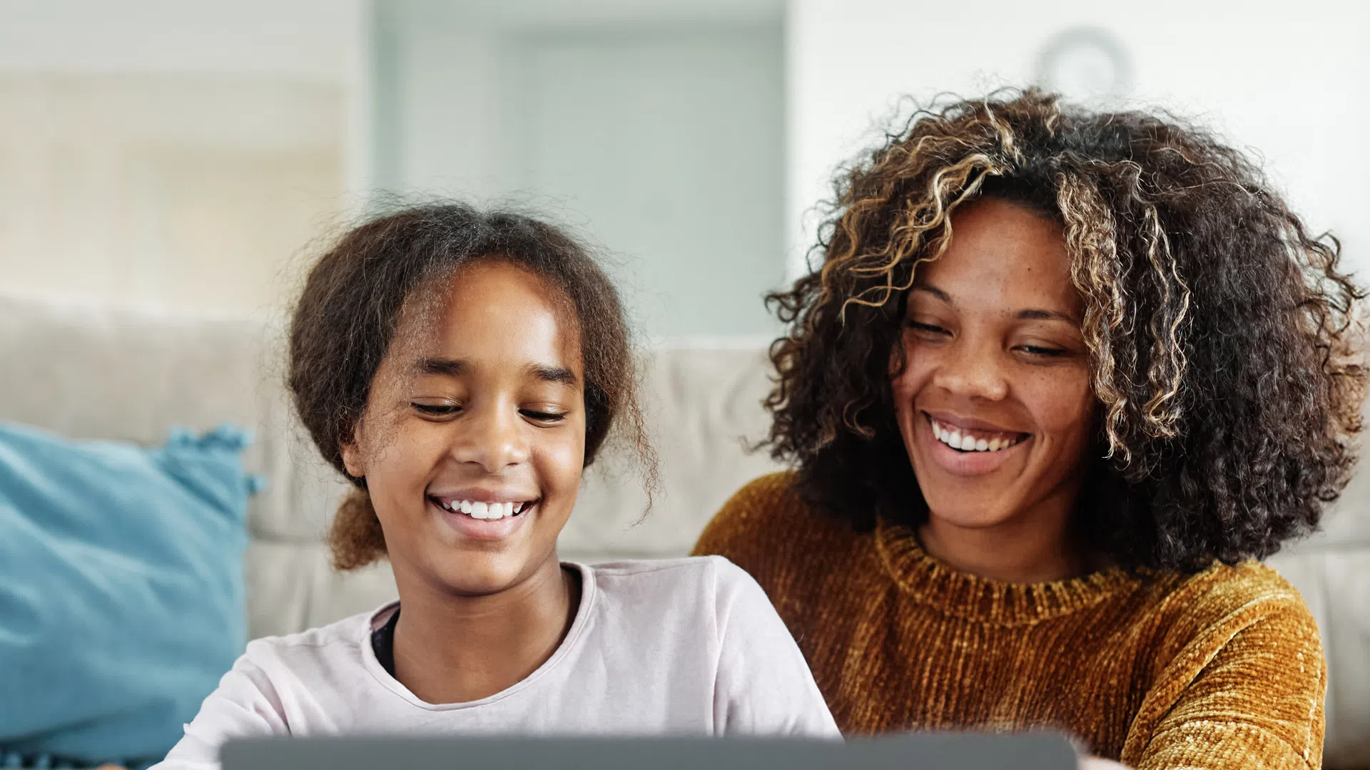 Smiling mother and daughter using laptop together on couch in cozy living room.