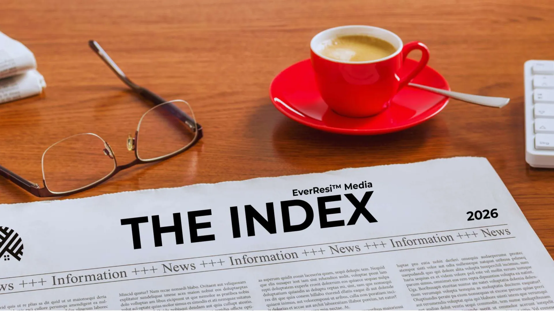 Newspaper labeled THE INDEX 2026 on desk with glasses, red espresso cup, keyboard, and pen nearby.