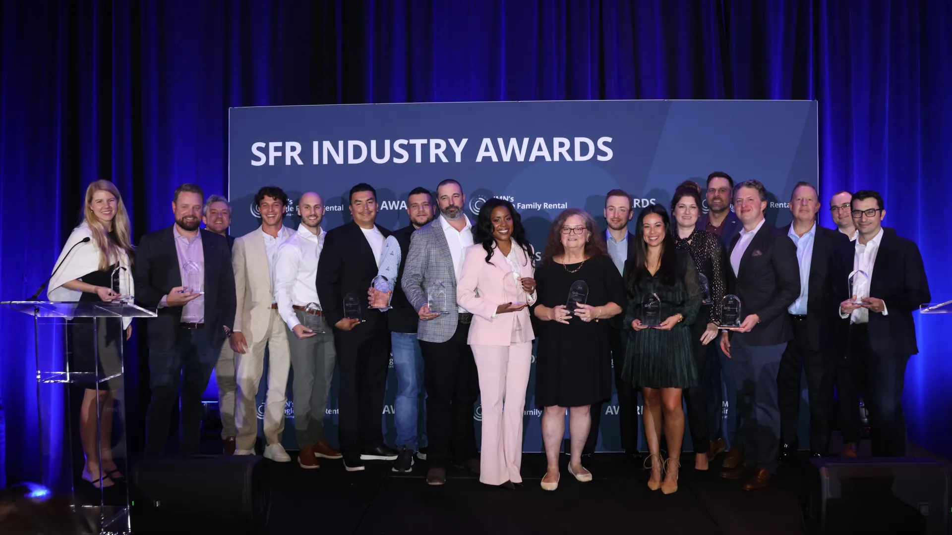 Group of diverse professionals holding awards at the SFR Industry Awards ceremony with blue backdrop and stage lighting.