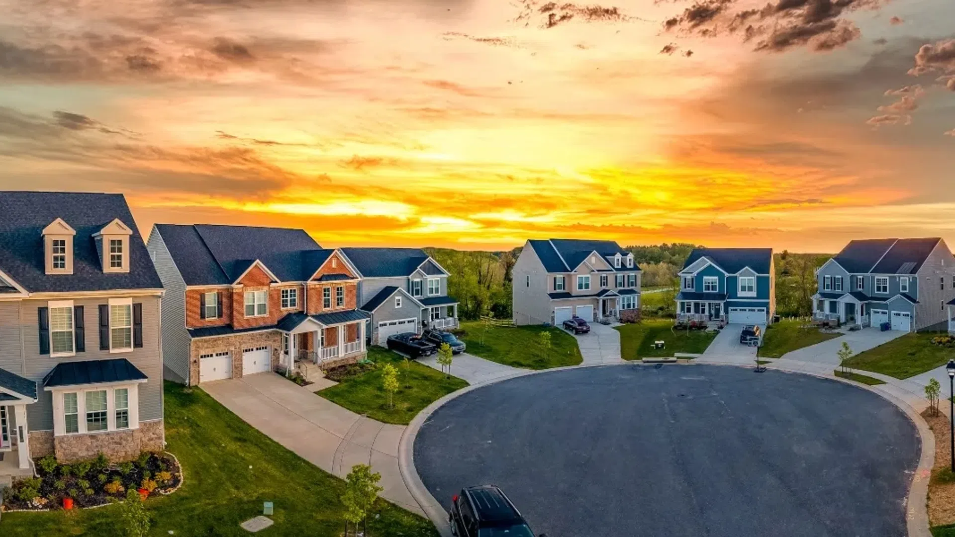 Sunset view of a suburban neighborhood cul-de-sac with modern two-story houses and well-kept lawns.