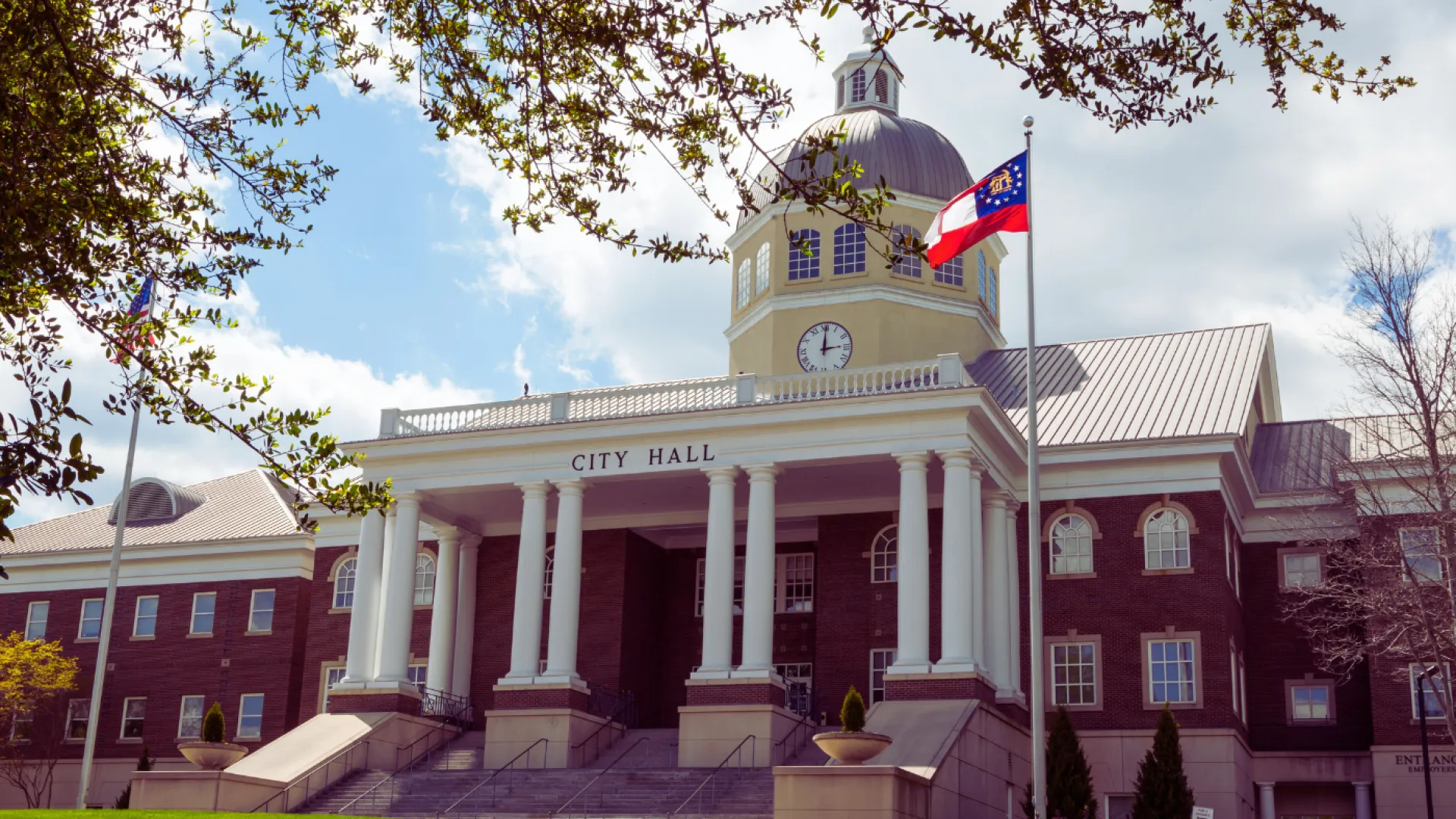 Historic city hall building with clock tower and American flag under a partly cloudy sky.