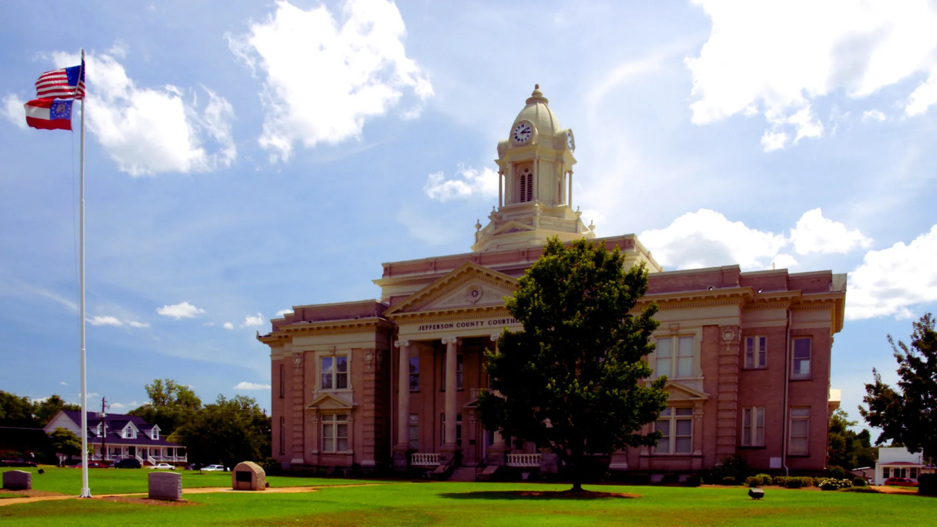 Historic Jefferson County Courthouse with clock tower under blue sky and flags flying on lawn