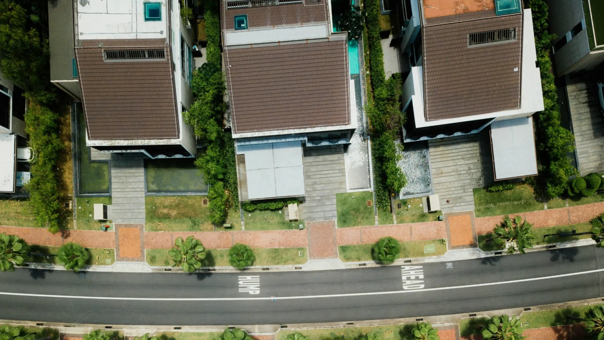 Aerial view of a suburban neighborhood with numerous houses, green trees, and roads under a golden sunlight.