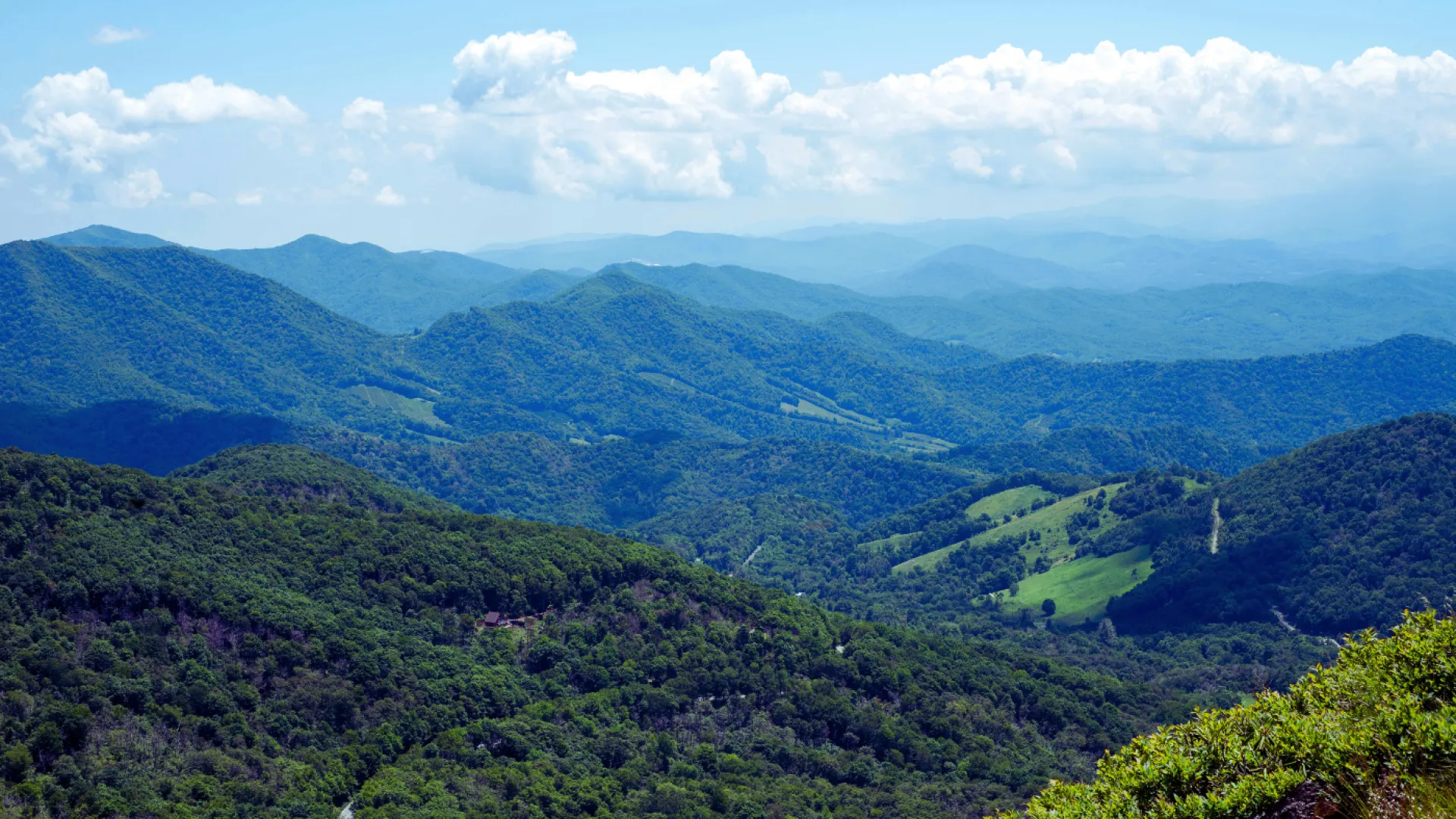 Panoramic view of green forested mountains under a blue sky with scattered clouds