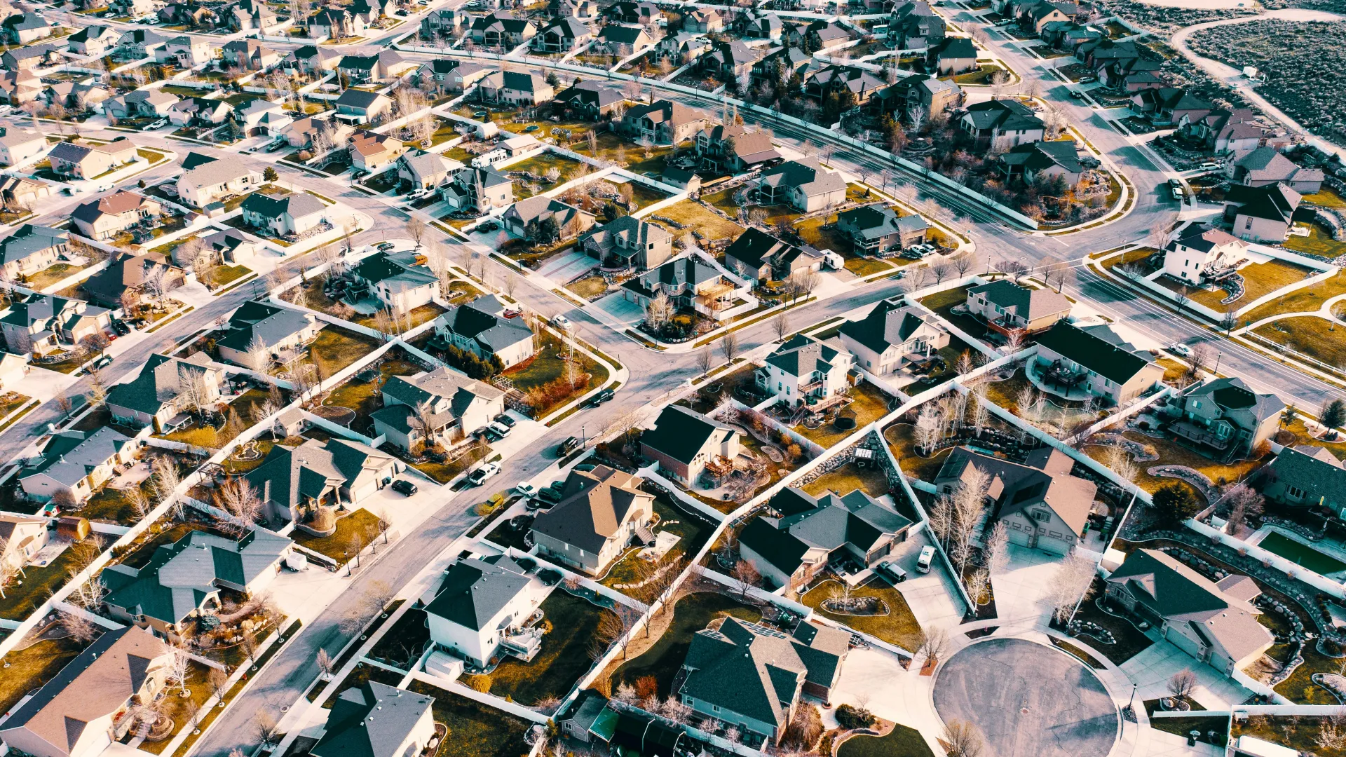 Aerial view of a suburban neighborhood with houses, curved roads, and a cul-de-sac under clear skies.