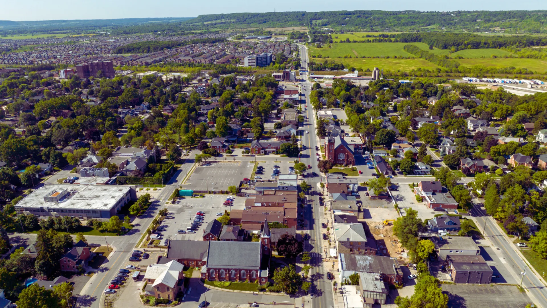 Aerial view of a suburban town with residential homes, churches, parking lots, and green fields in the distance.