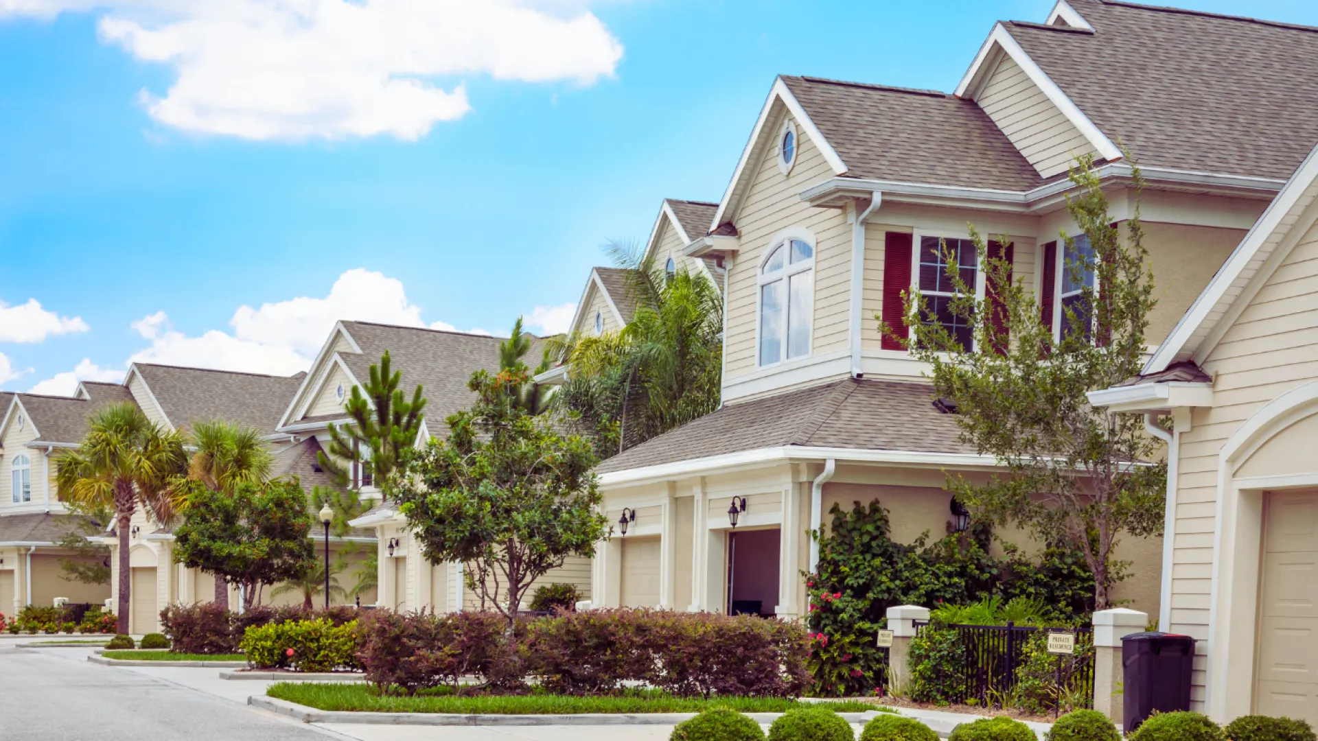 Row of modern suburban two-story houses with manicured lawns under a blue sky with clouds