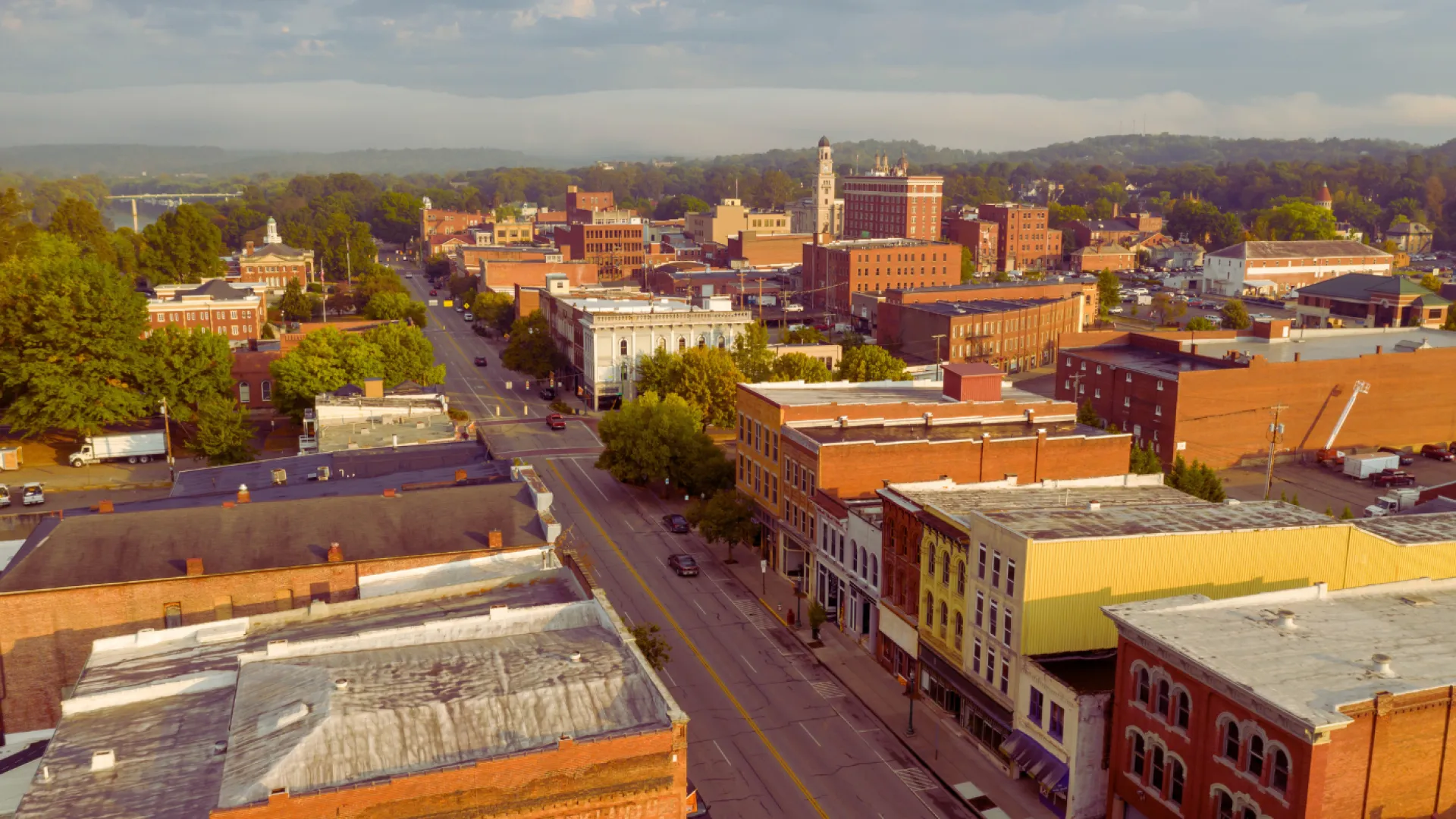 Aerial view of a small city's downtown with historic brick buildings and tree-lined streets at sunset.