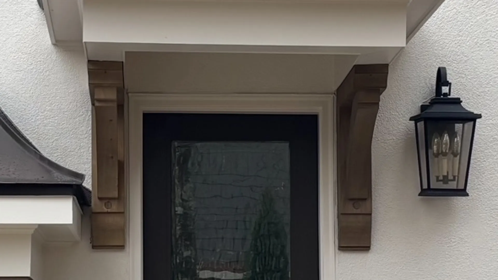 Modern black front door with textured glass, covered porch, black railing, and exterior wall lantern on white stucco