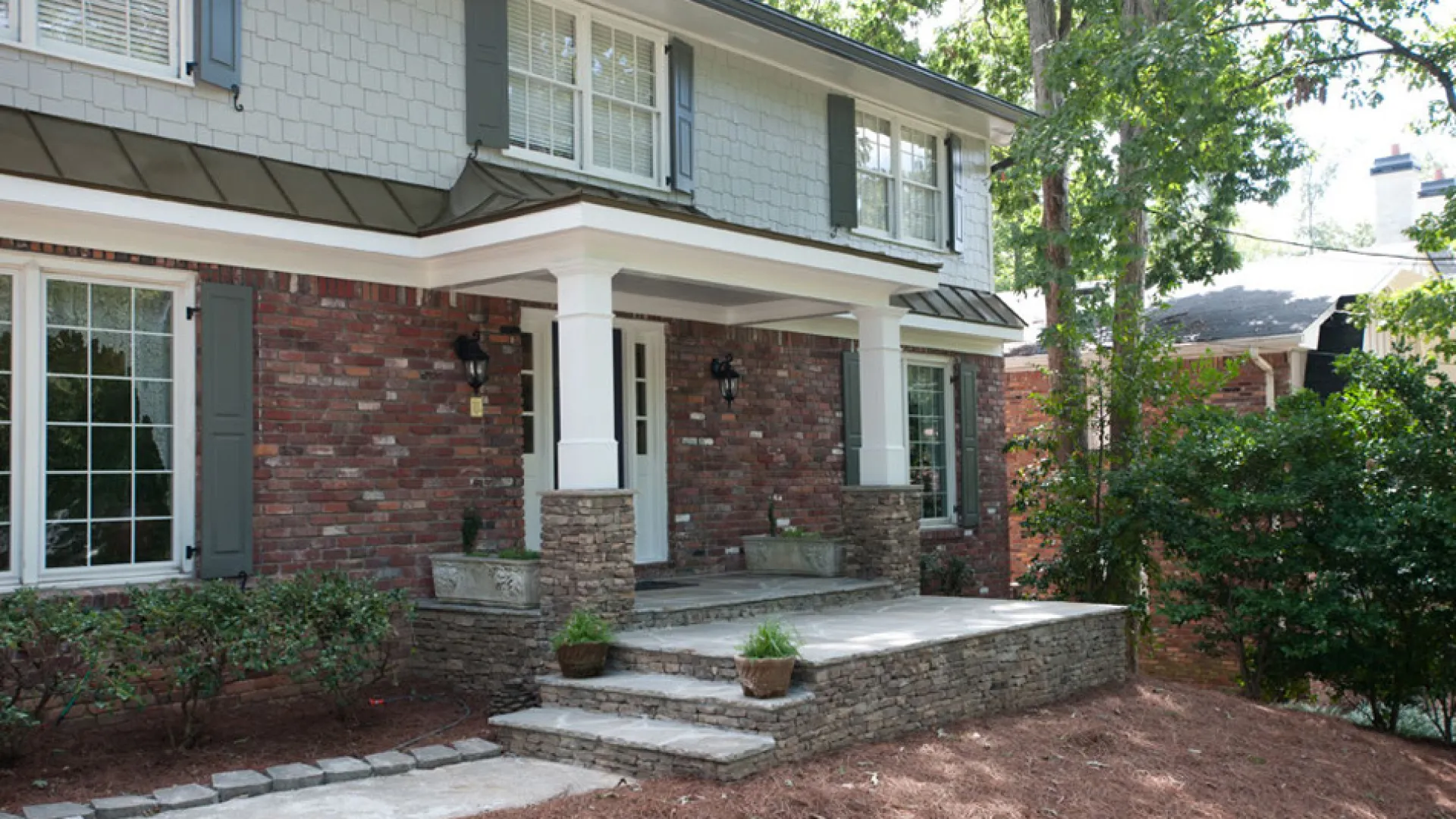 Charming exterior of a brick house with a stone walkway, lush greenery, and inviting porch.