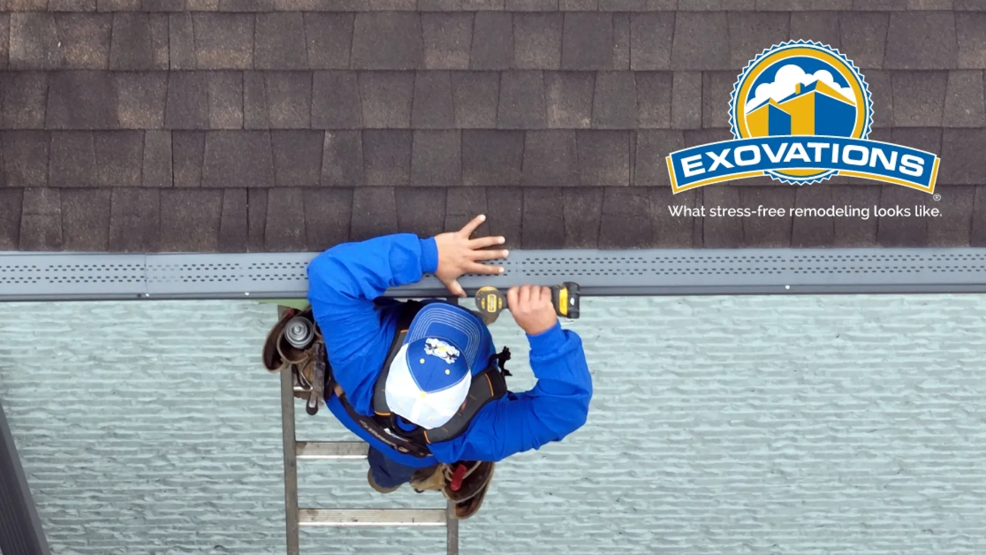 Roofer in blue shirt and cap installing gutter on shingled roof viewed from above with Exovations logo.