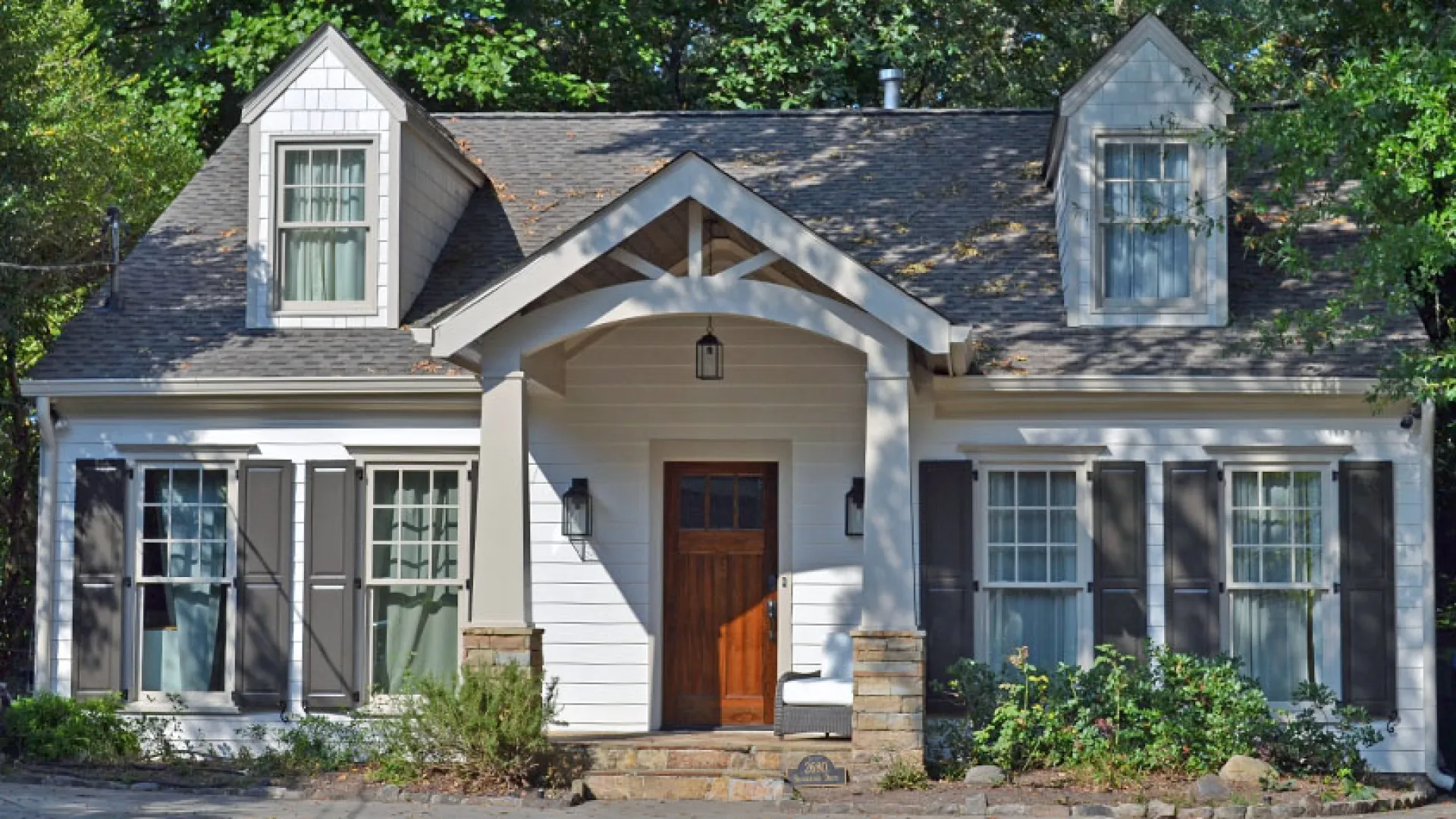 Charming white cottage with a gabled roof surrounded by greenery and a stone pathway.