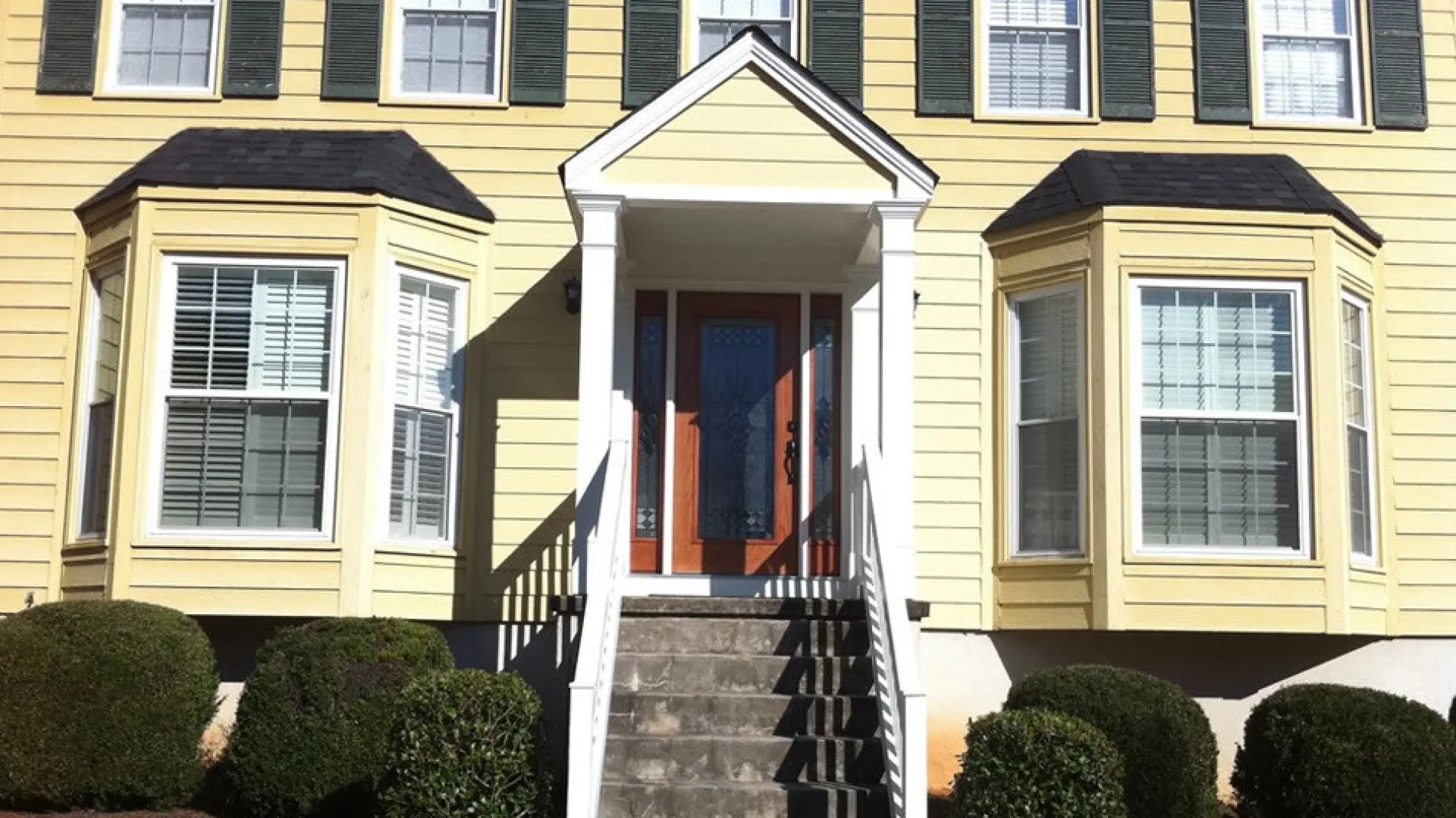 Charming yellow house with bay windows and a welcoming front porch entryway.