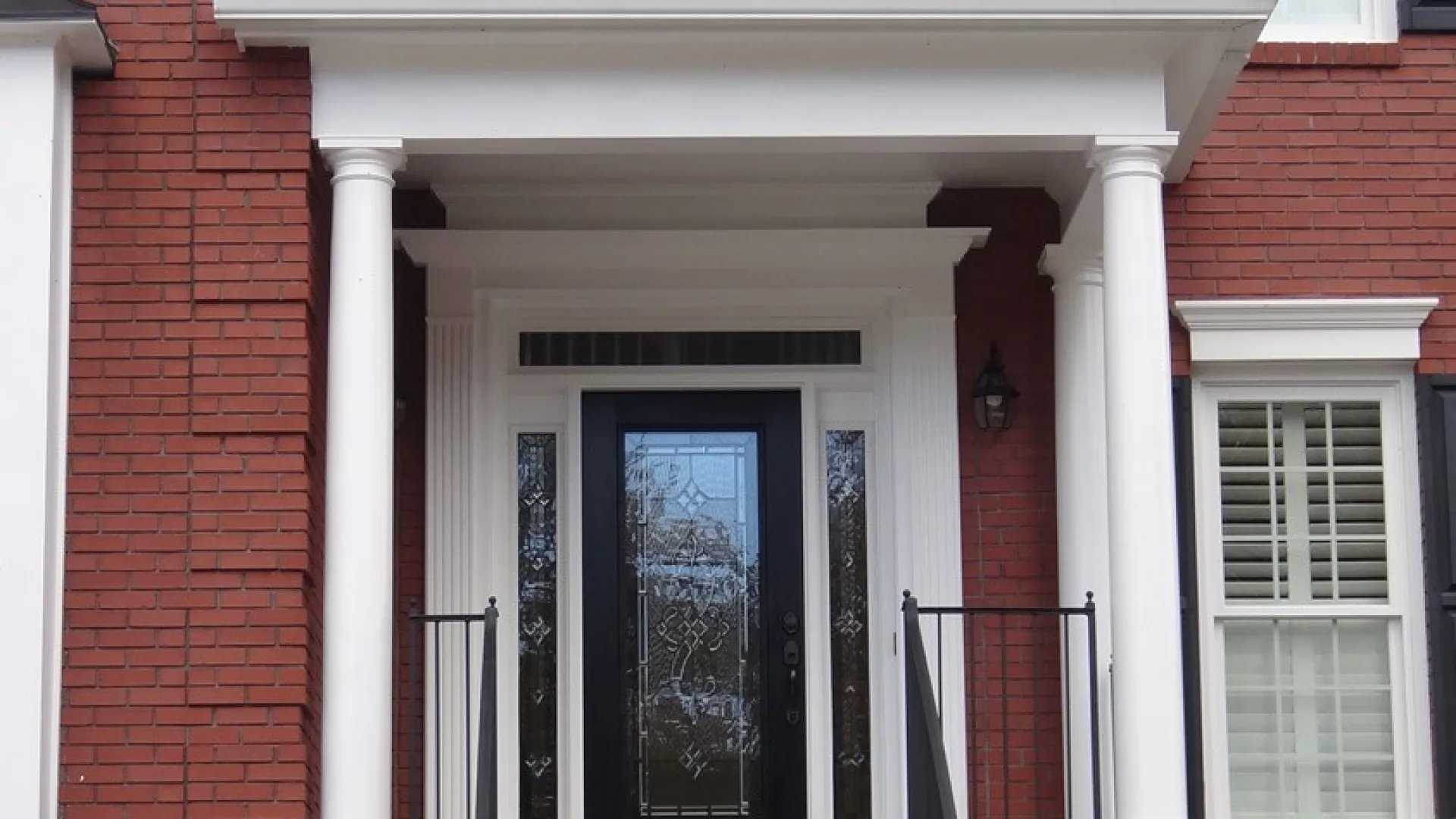 Elegant brick house entrance featuring a black door with decorative glass and white columns.